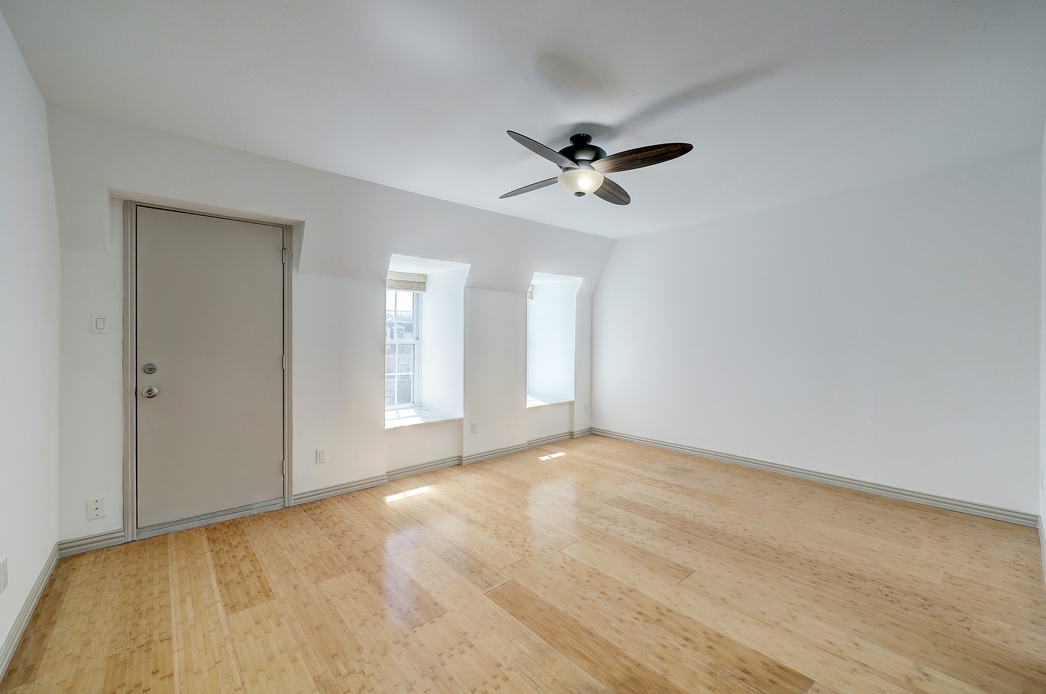 A sizable bedroom offers durable wood-like flooring, and a ceiling fan with light kit. Large windows flood the room with natural light, while the window sitting doubles as storage space. Door pictured on the left offers direct access to a shared balcony space.