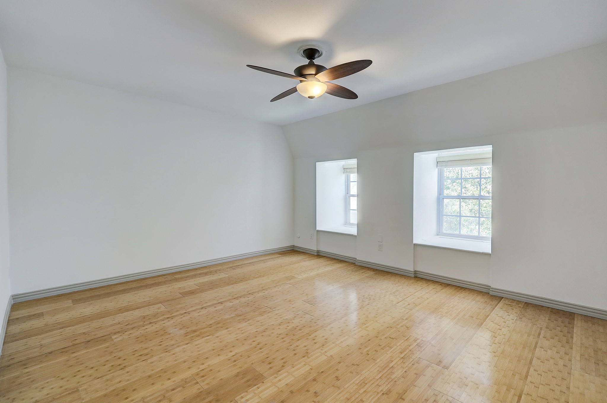 A sizable bedroom offers durable wood-like flooring, and a ceiling fan with light kit. Large windows flood the room with natural light, while the window sitting doubles as storage space.