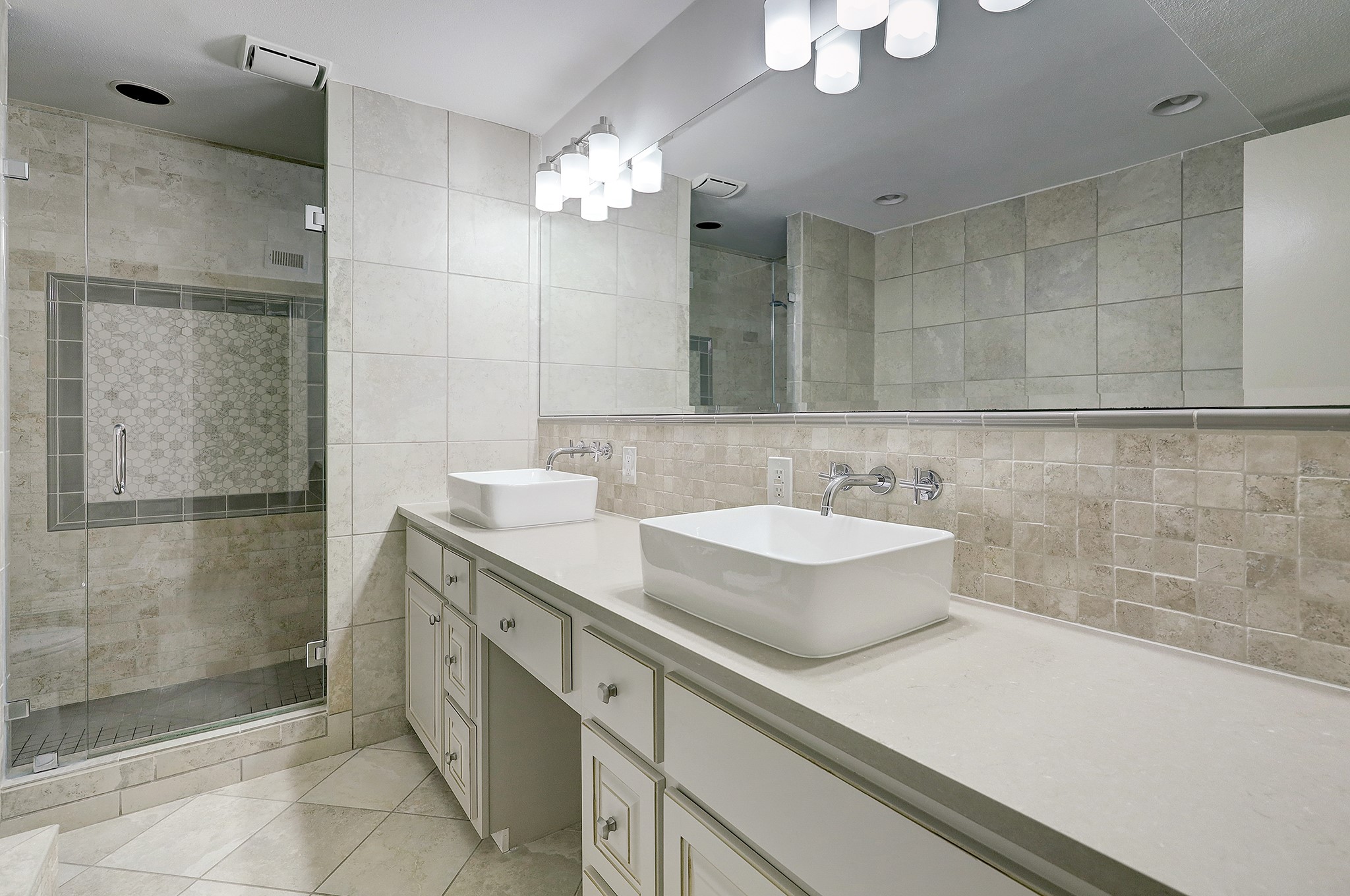 A tribute to elegance in design, expansive light gray countertops and white vessel sinks, are complemented by wall-mounted chrome fixtures. Ample cabinetry space offers abundant storage.