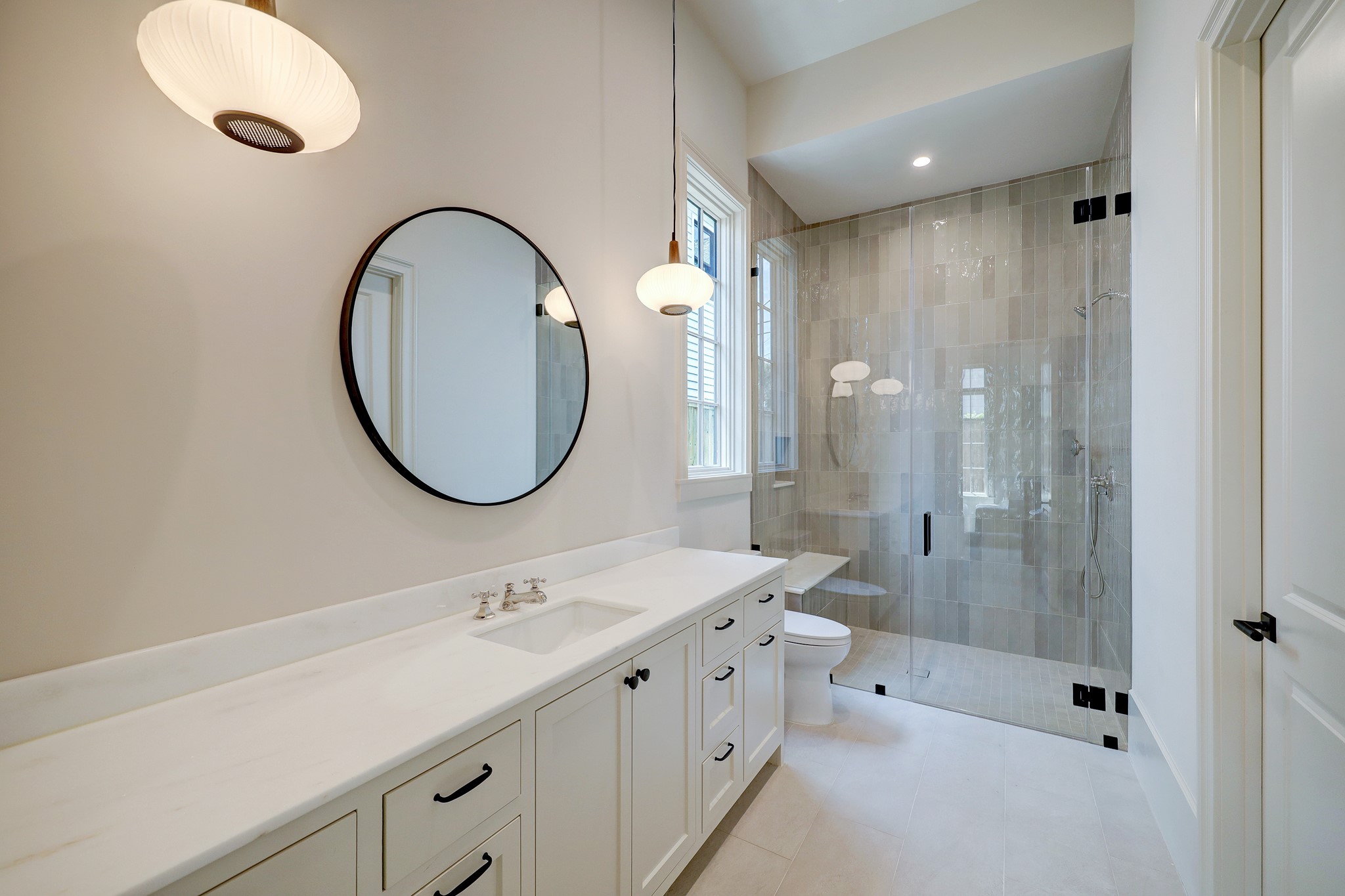 En suite bathroom to the first floor guest bedroom offers a walk-in shower with ceramic tile, bench seat and seamless glass door. Designer pendants illuminate the space.