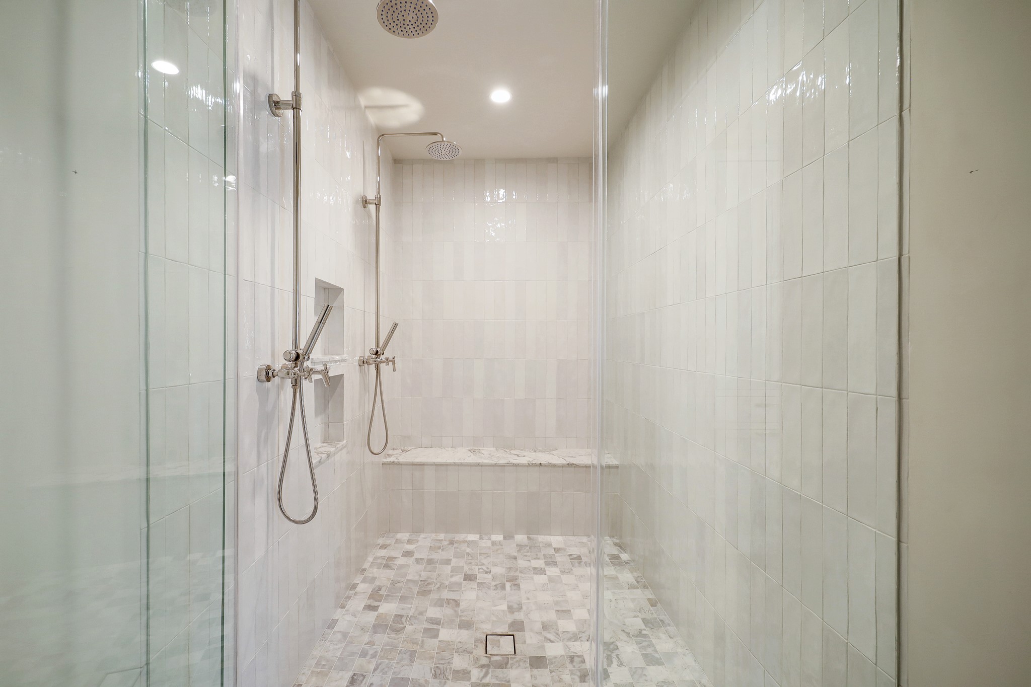 Spacious walk-in shower with curb-less entry, framless glass door, floor to ceiling Ceramic Zellige look tile, two rain shower heads and bench seat. Every detail is well thought out.