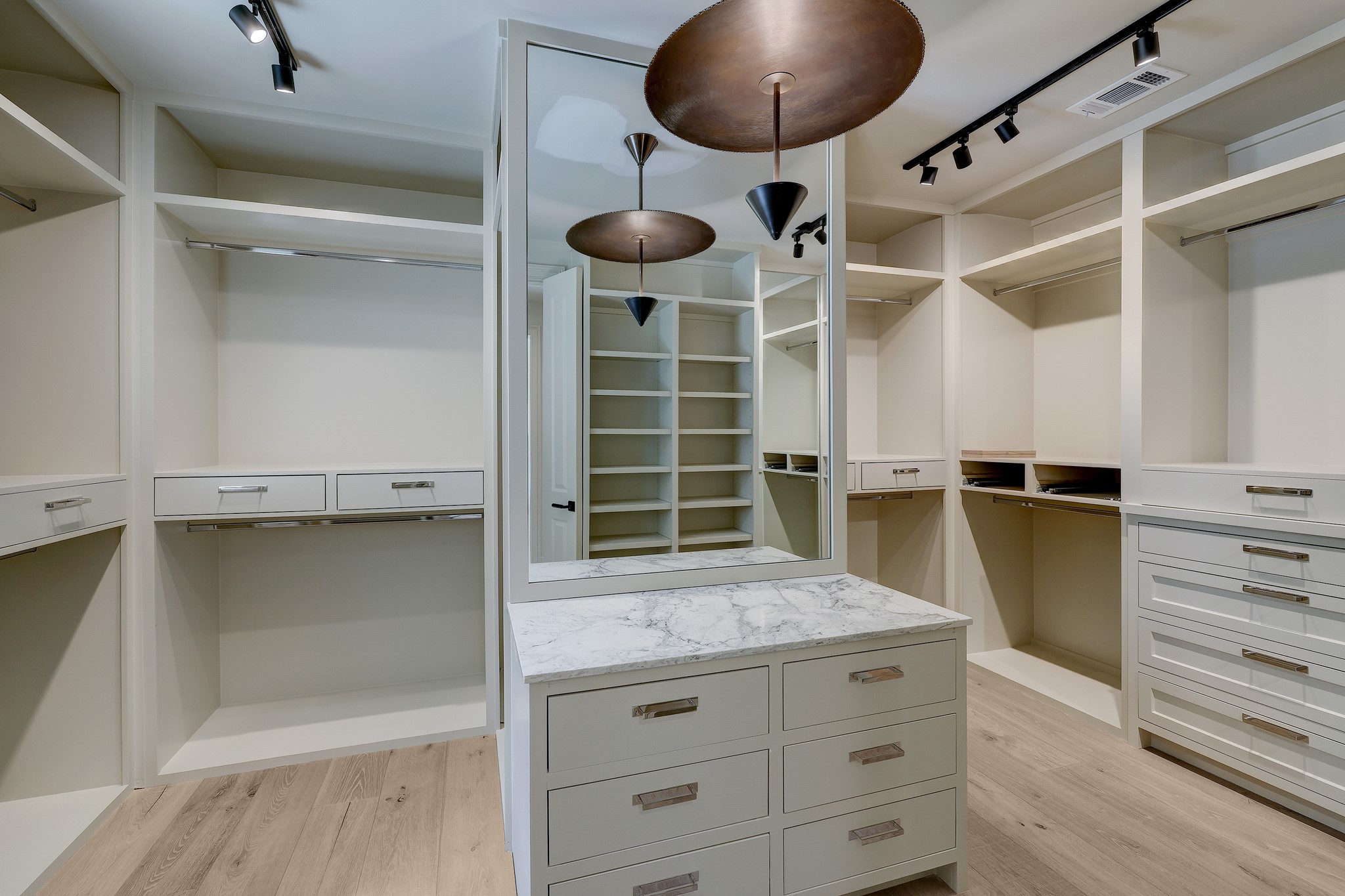 Walk-in closet with dual sides, custom built ins and packing island and mirror. Track lighting and designer pendant illuminate this fabulous space to get ready.