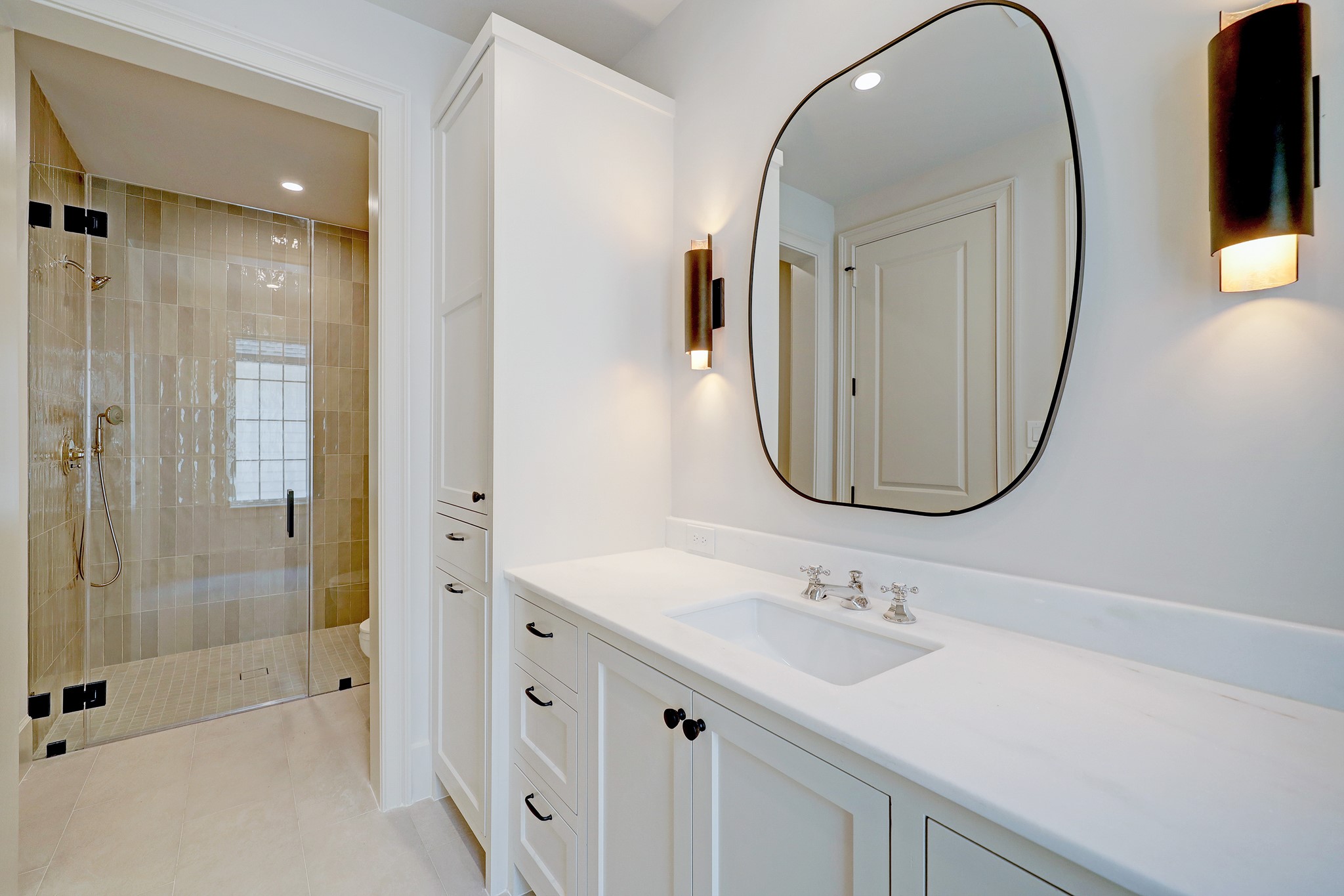 En suite bathroom with designer lighting, Noble white marble countertops and black cabinetry hardware.