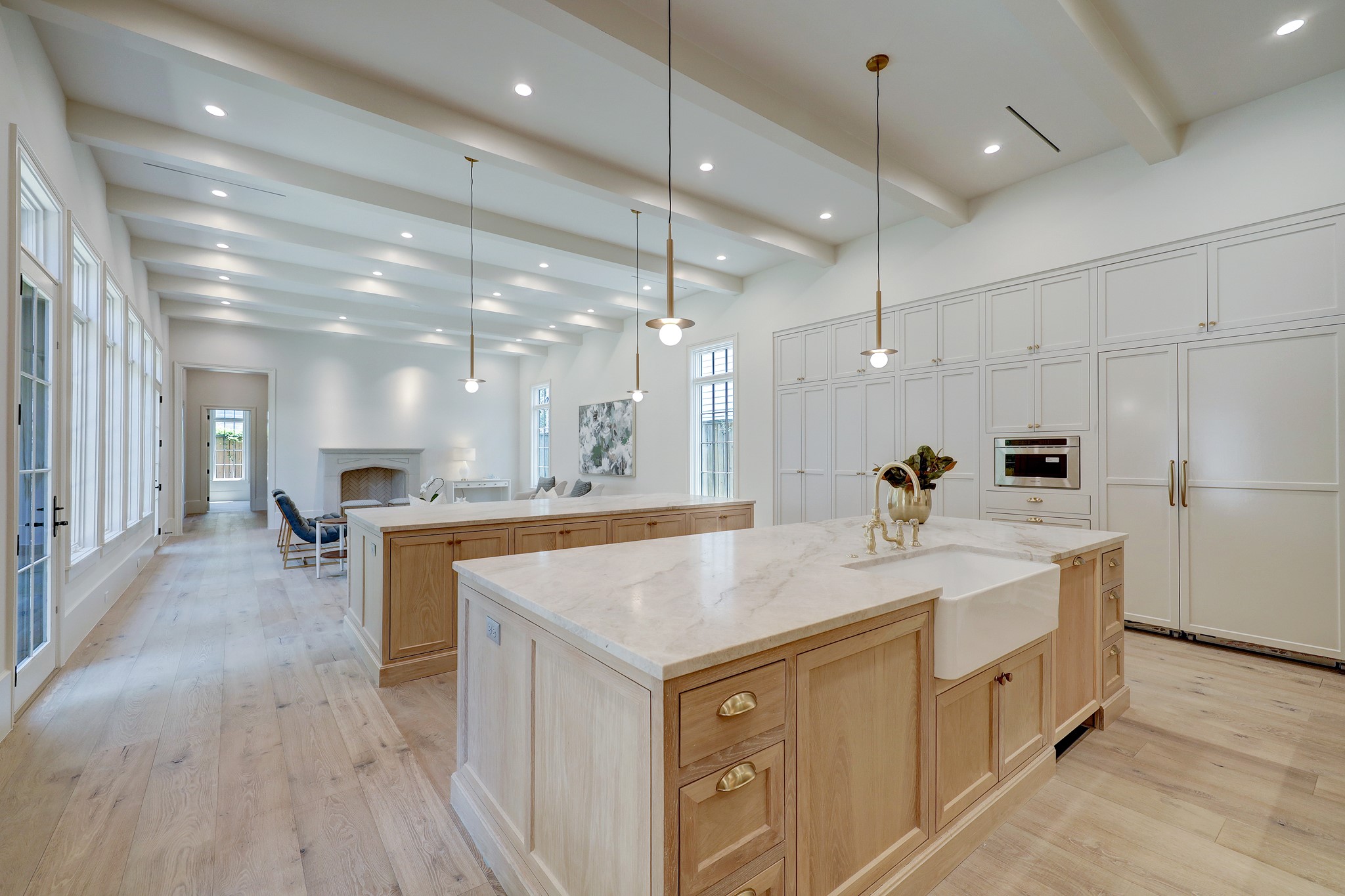 Stunning chef's kitchen with two islands with white oak cabinetry, Tahj Mahal quartzite countertops, fleet of upscale appliances, and satin brass cabinet hardware.