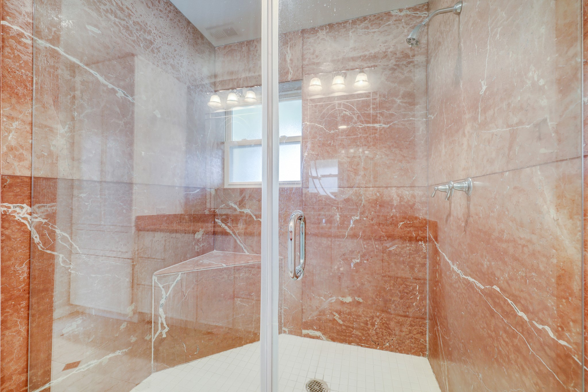 Large marble shower with glass enclosure and bench seat.