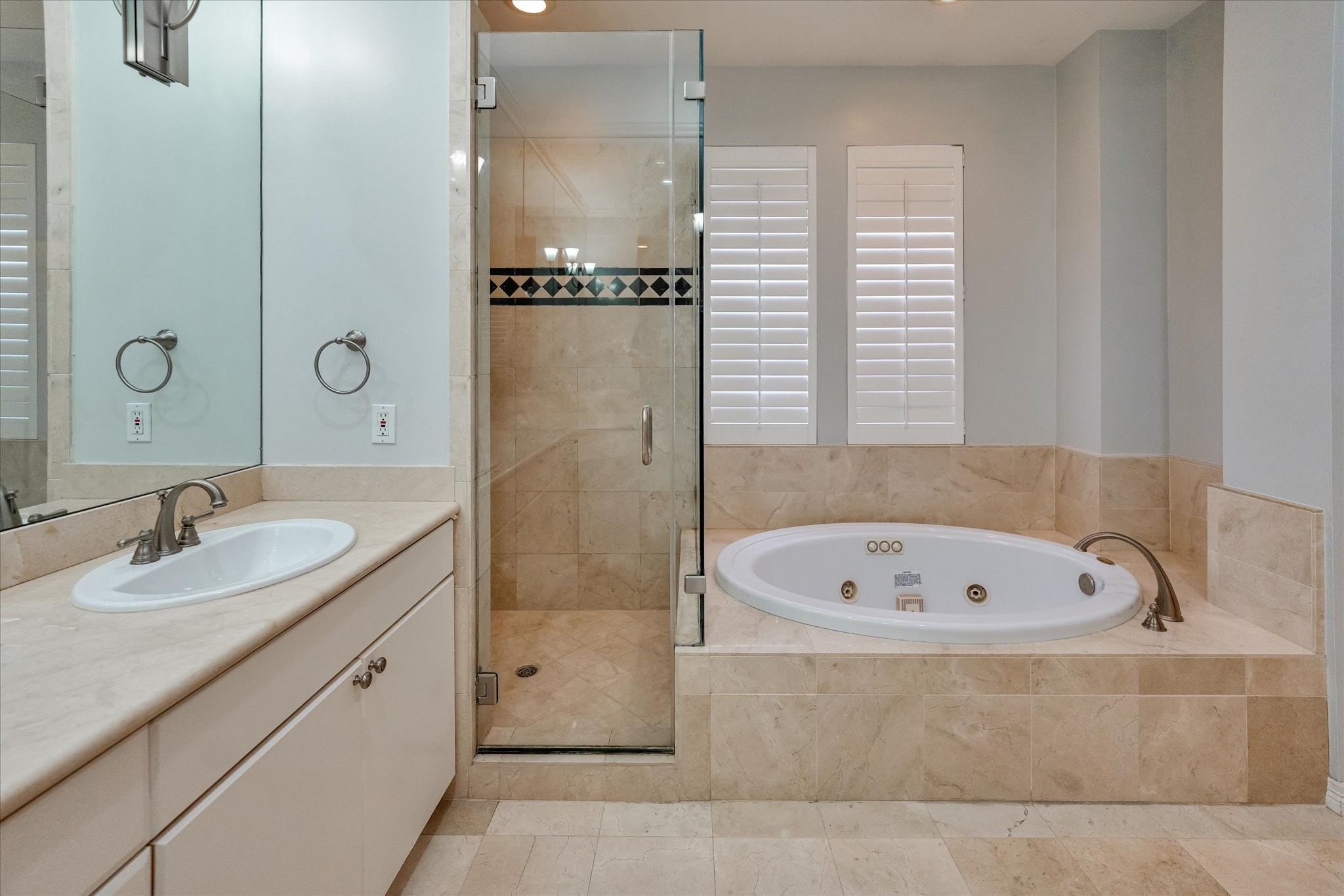 A closer view of your seamless glass walk-in shower and sizable jetted tub, with privacy shuttered windows.