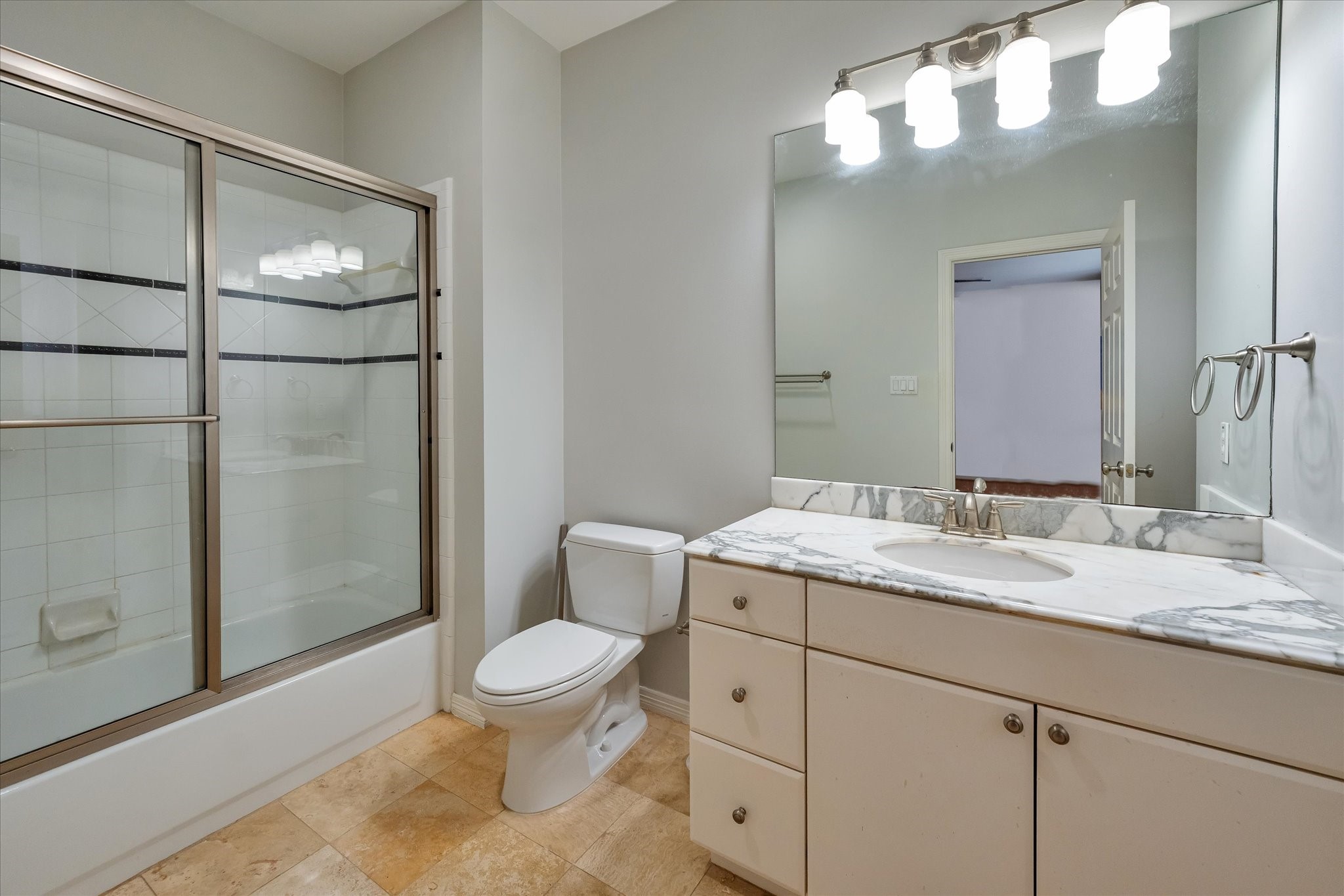 Enter your secondary en suite bath, fitted with tile flooring, an updated lighting fixture, a tub/shower combo equipped with a glass shower door, and a single vanity design.