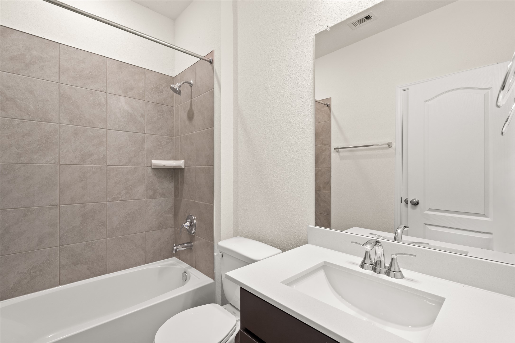 Secondary bath features tile flooring, bath/shower combo with tile surround, dark wood cabinets, beautiful light countertops, mirror, dark, sleek fixtures and modern finishes.
