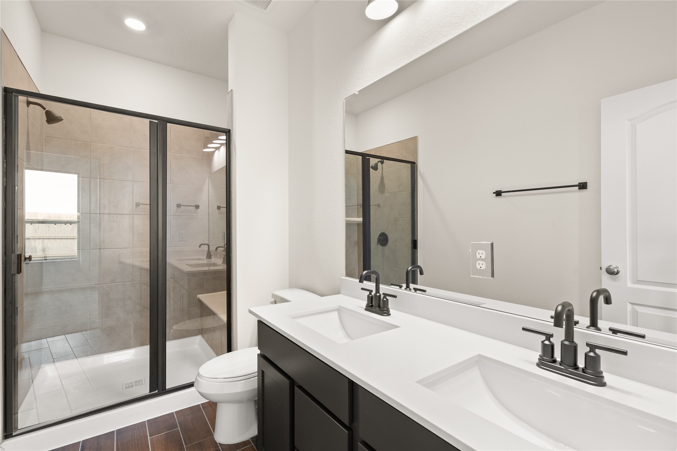 This primary bathroom is definitely move-in ready! Featuring a dark framed walk-in shower with tile surround, dark stained cabinets with light countertops, spacious walk-in closet with shelving, high ceilings, custom paint, sleek and dark modern finishes.
