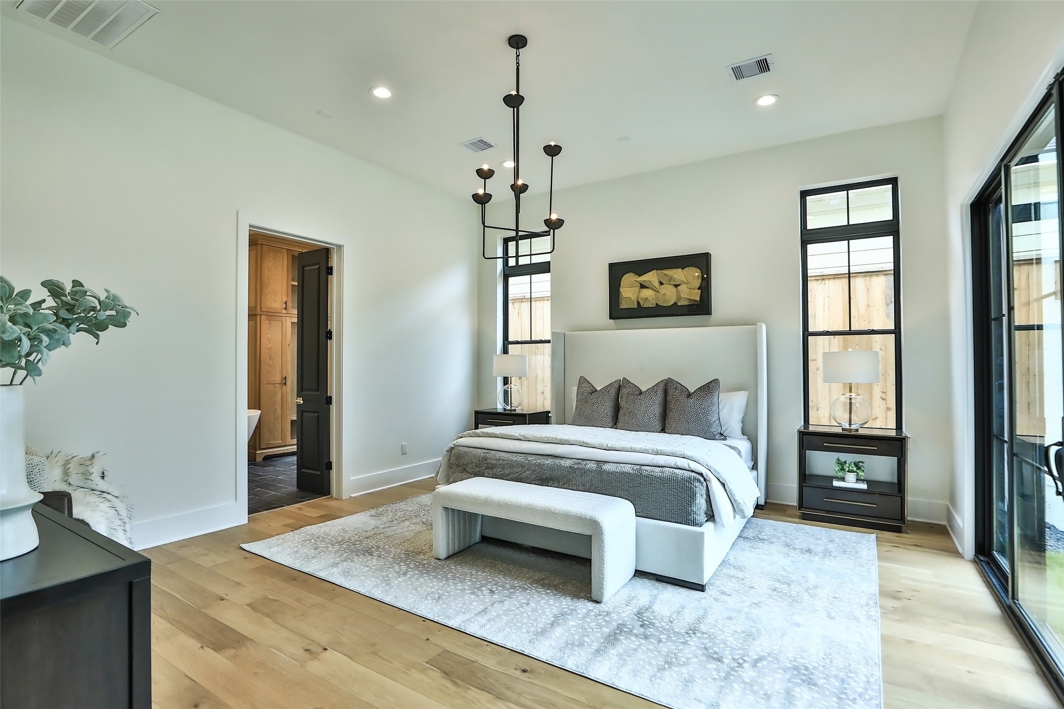 The primary bedroom is in a private location in the back of the home. The room features a classic hammered wrought iron chandelier and White Oak Engineered hard wood floors.