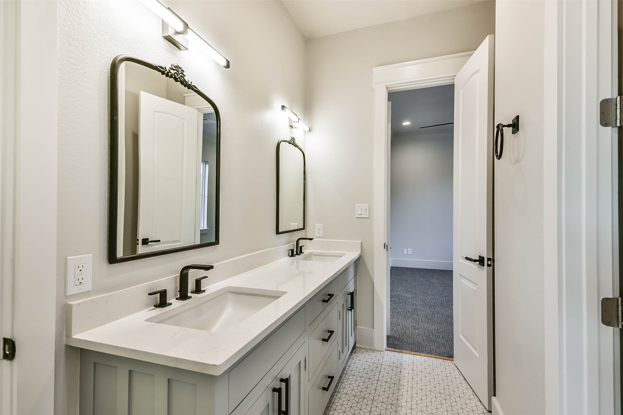 Secondary bath with double sinks hung mirrors and decorative tile floor connect bedrooms two and three.