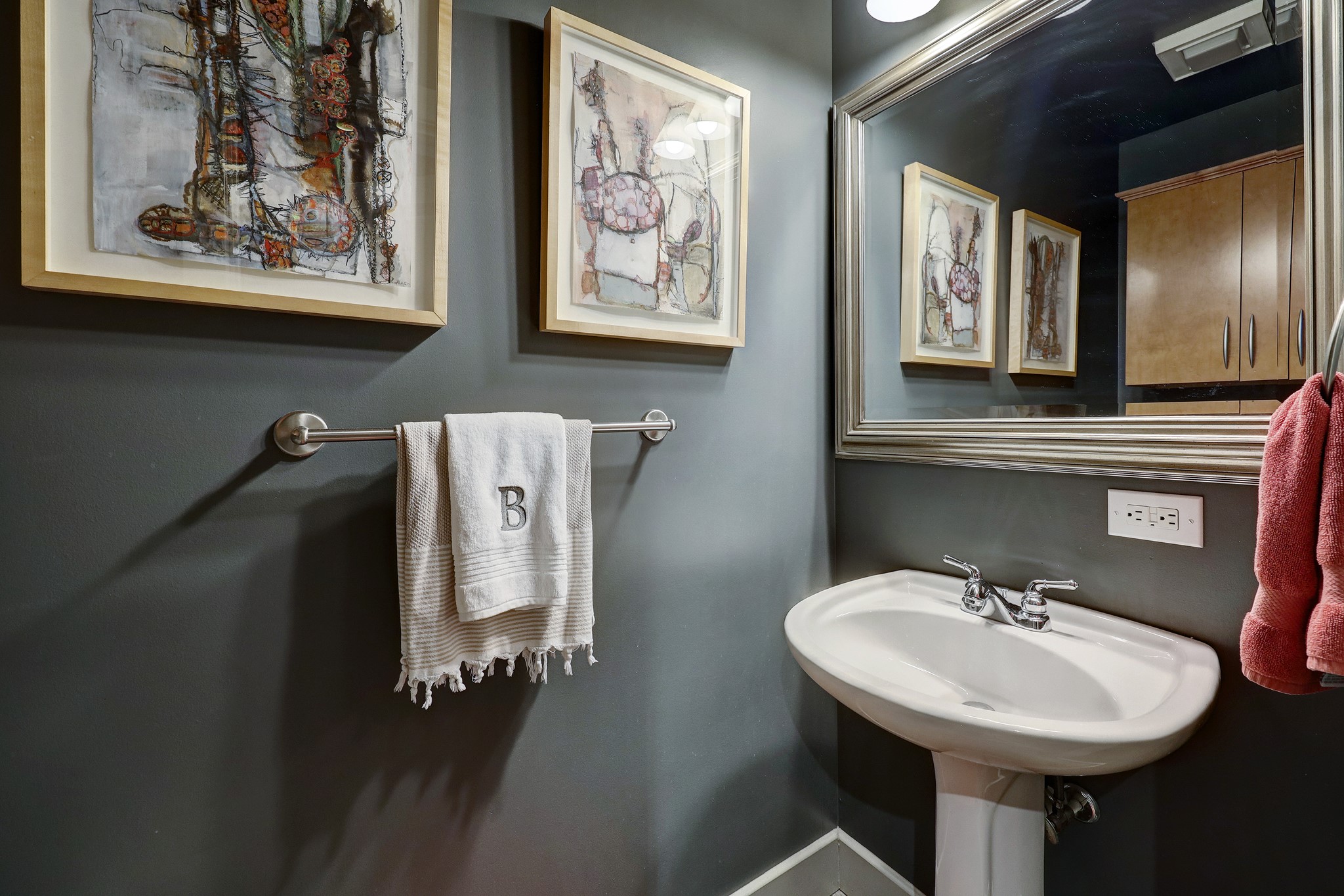 The powder room is conveniently located off the foyer and features a pedestal sink, a beautifully framed mirror and an overhead cabinet.