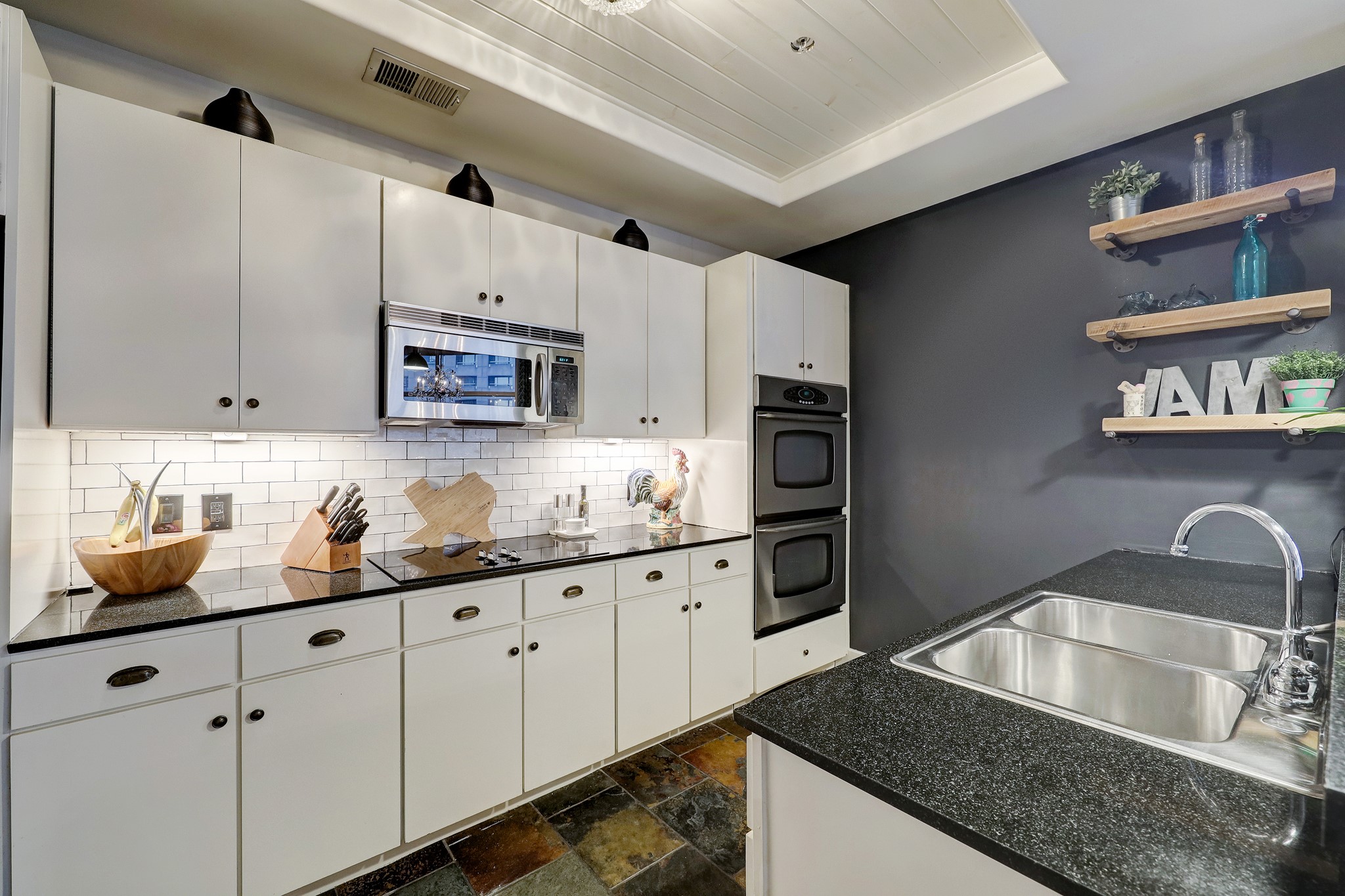 This modern kitchen features freshly painted cabinets, new hardware, white subway tile backsplash, magnet/chalkboard wall with wood shelving, slate tile flooring, elegant lighting and a wood recessed ceiling.