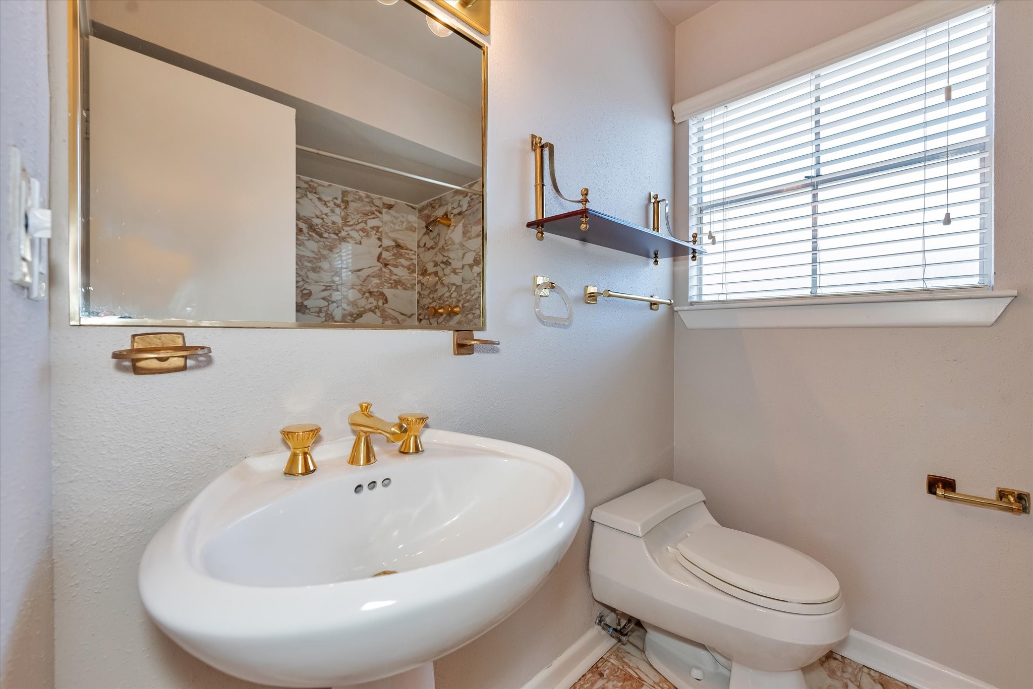Hall bath has pedestal sink, marble tile, gold fixtures.