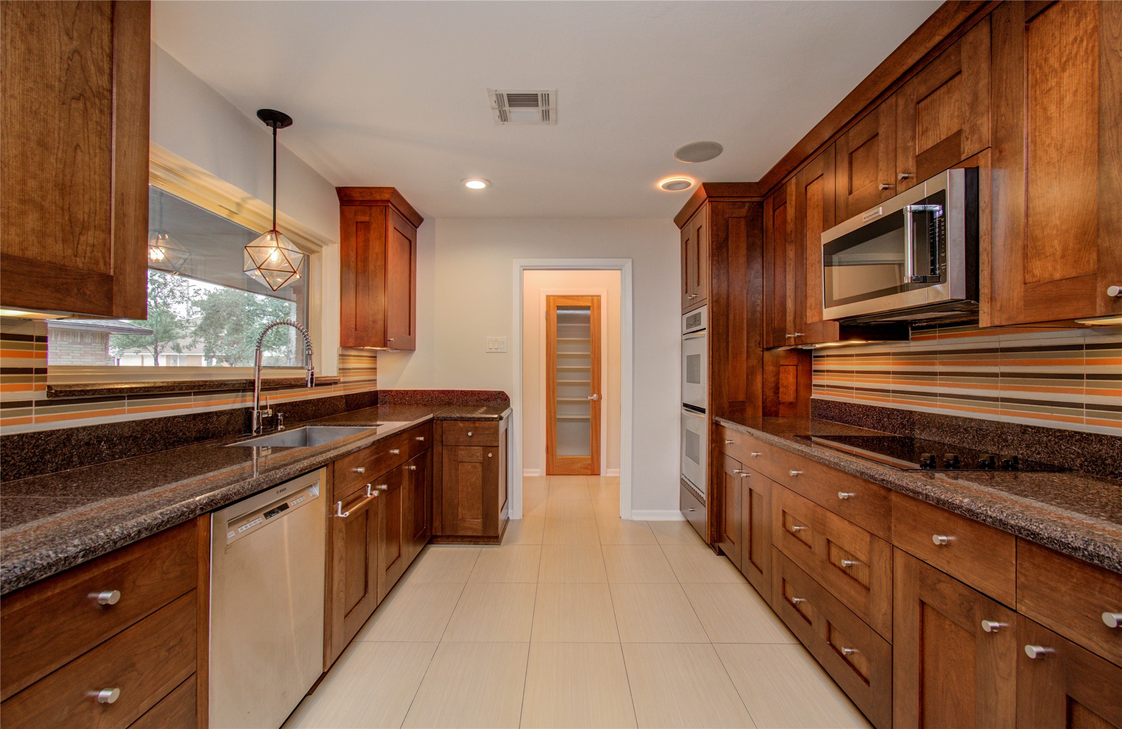 The kitchen showcases top-tier stainless steel appliances. Yet, even with these contemporary enhancements, the owners skillfully maintained the room's standout feature: a distinctively captivating backsplash that harmoniously contrasts the warm, rich tones of the wooden cabinets.