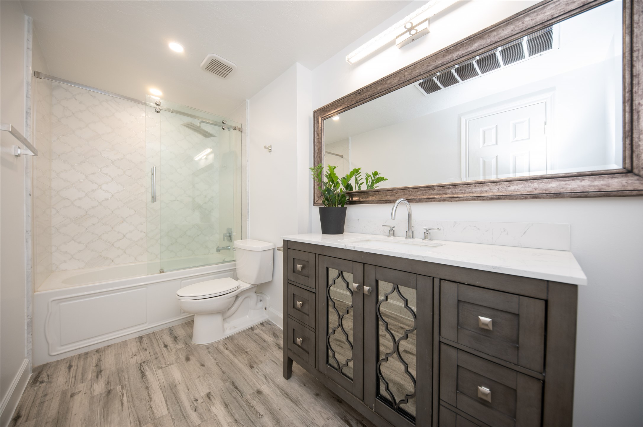 Here is a great angle on this updated bathroom with a custom furniture bathroom sink & soft close drawers, large framed mirror and custom bathtub/shower combination featuring frameless glass. Notice the wood 