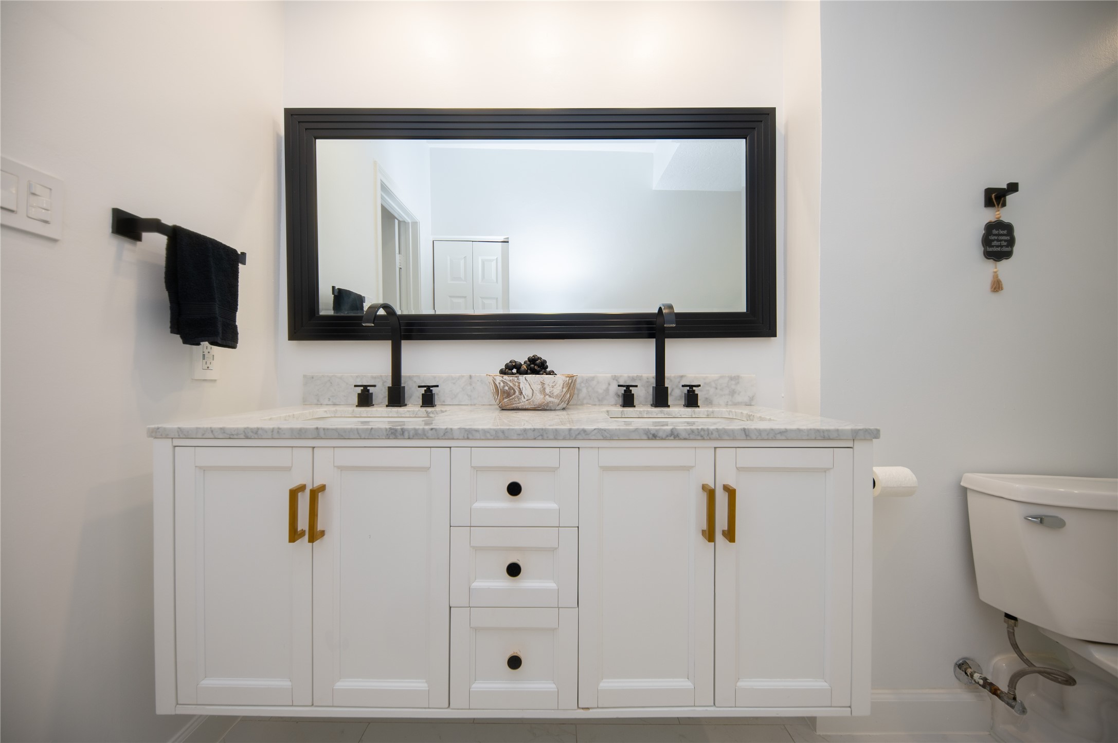 Welcome to this updated primary bathroom. This full on shot highlights the bathroom vanity with warm gold pull handles and black and gold drawer pulls.