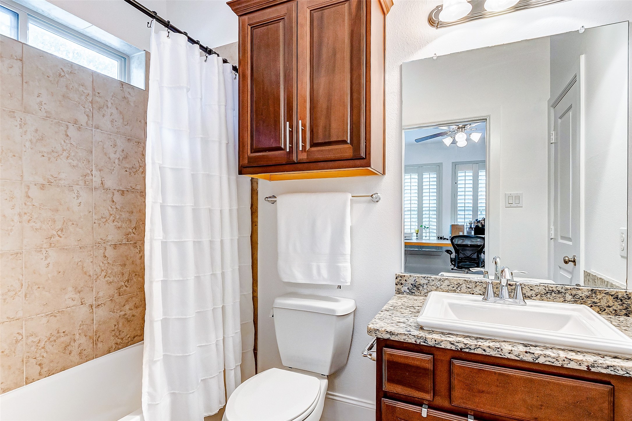 The first floor bedroom offers its own private bathroom featuring granite countered vanity, shower/tub combo with tile surround, rich cabinetry, and nickel fixtures.