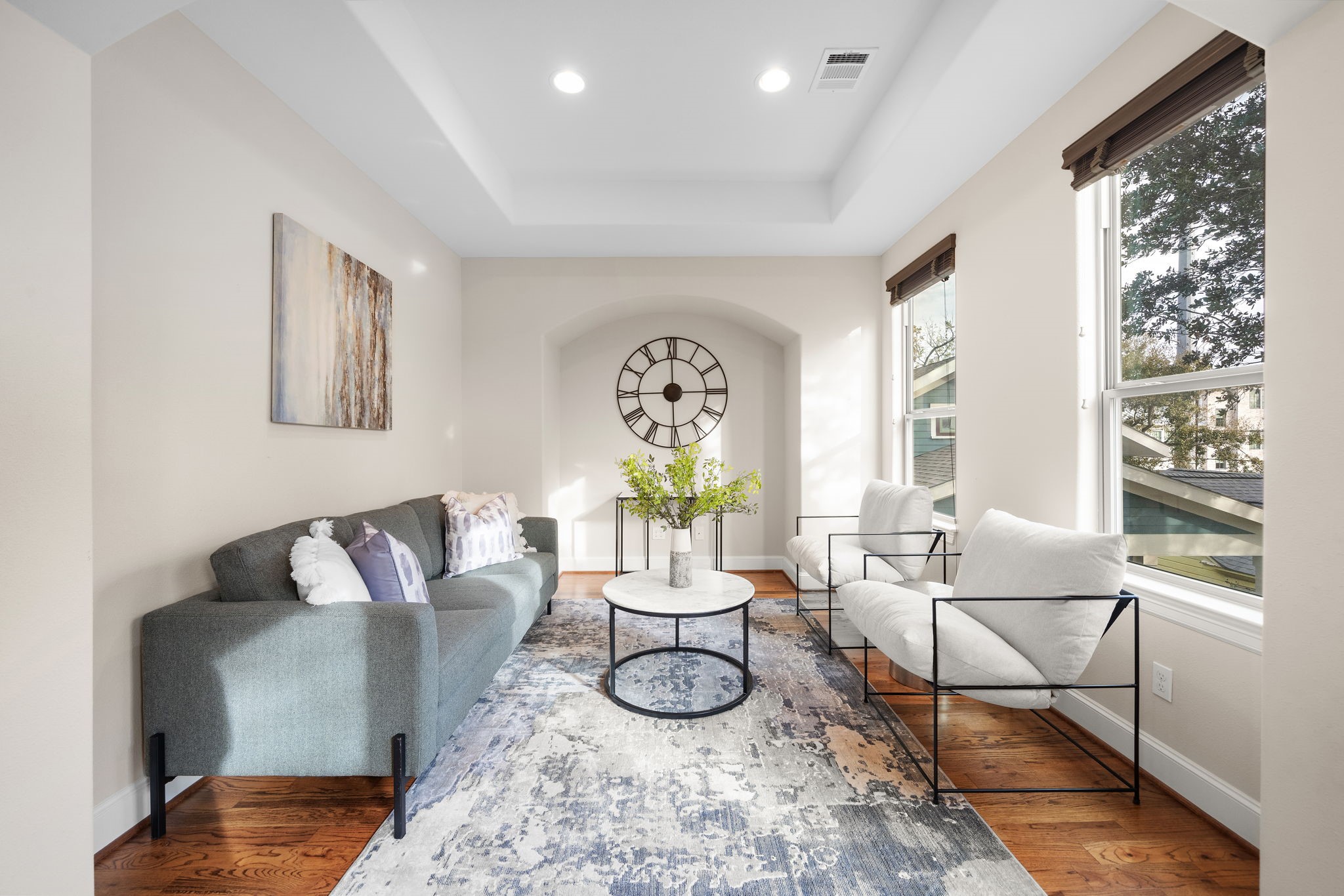 Bright and airy, the primary suite's seating area showcases tray ceilings, a stylish arched inlet, hardwood floors, and generous space for multiple seating arrangements.