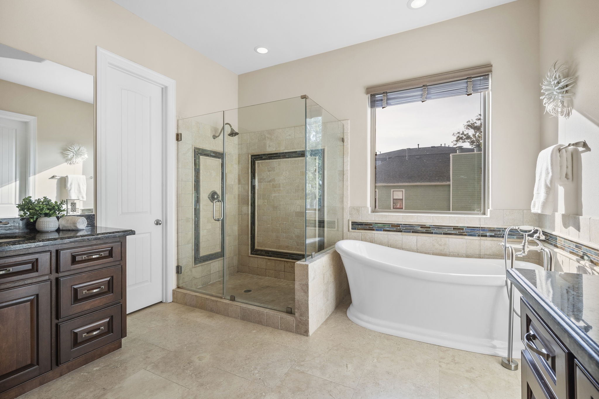 The luxurious primary ensuite bath showcases tile flooring, a water closet for privacy, abundant natural light cascading through the large window, and separate vanities fitted with granite countertops and built-in cabinets.