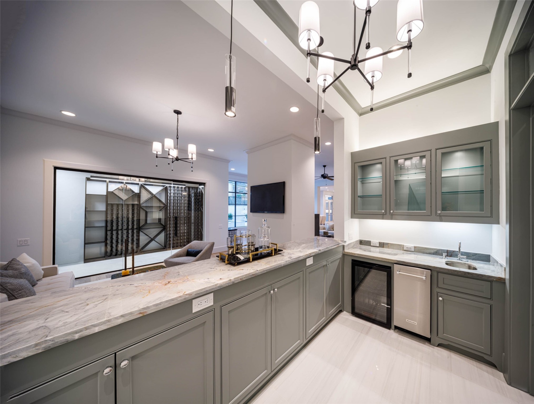 Spacious wet bar with built-in beverage and wine refrigerator, ice maker, sink, glass front cabinetry, designer chandelier and hanging pendants and above and under cabinet lighting