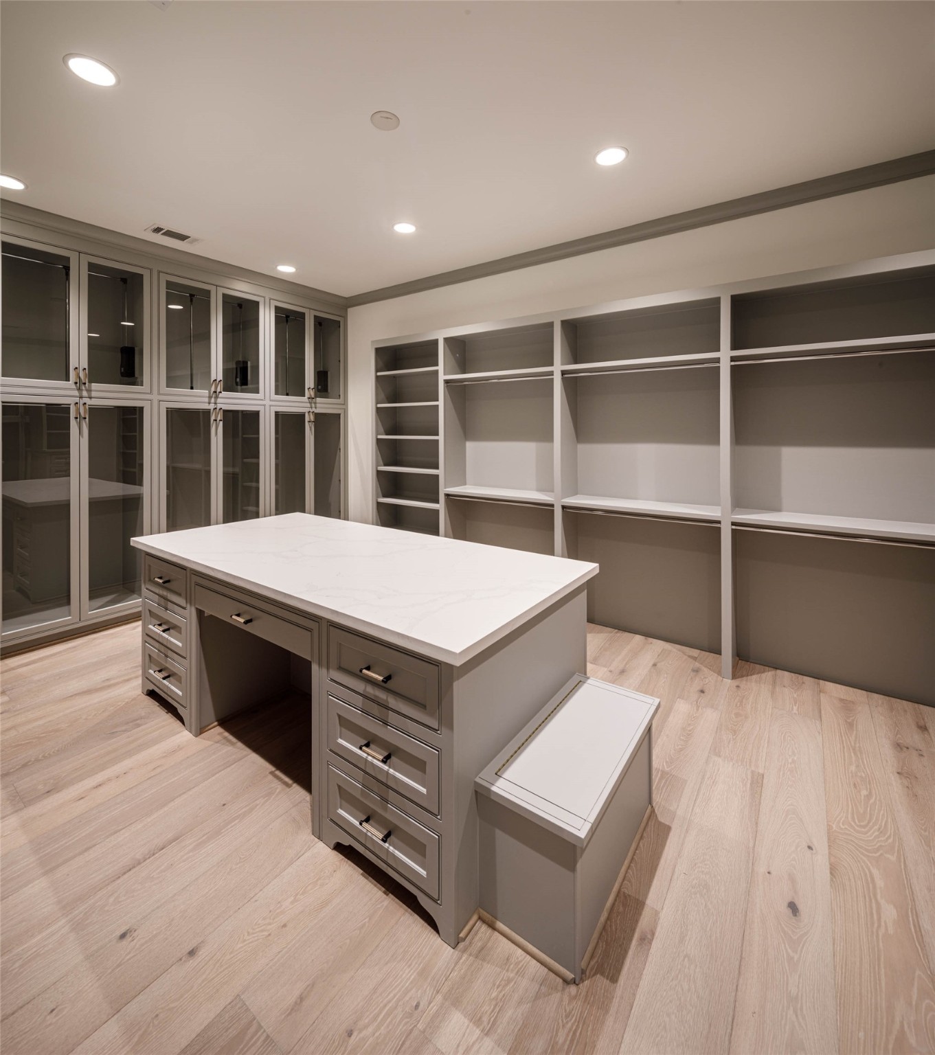 One of the Two primary dressing areas with engineered white Oak wood floors, furniture quality cabinetry, custom packing island with built-in storage, glass front cabinets with hanging rods, boutique style mirror and concealed security safety box