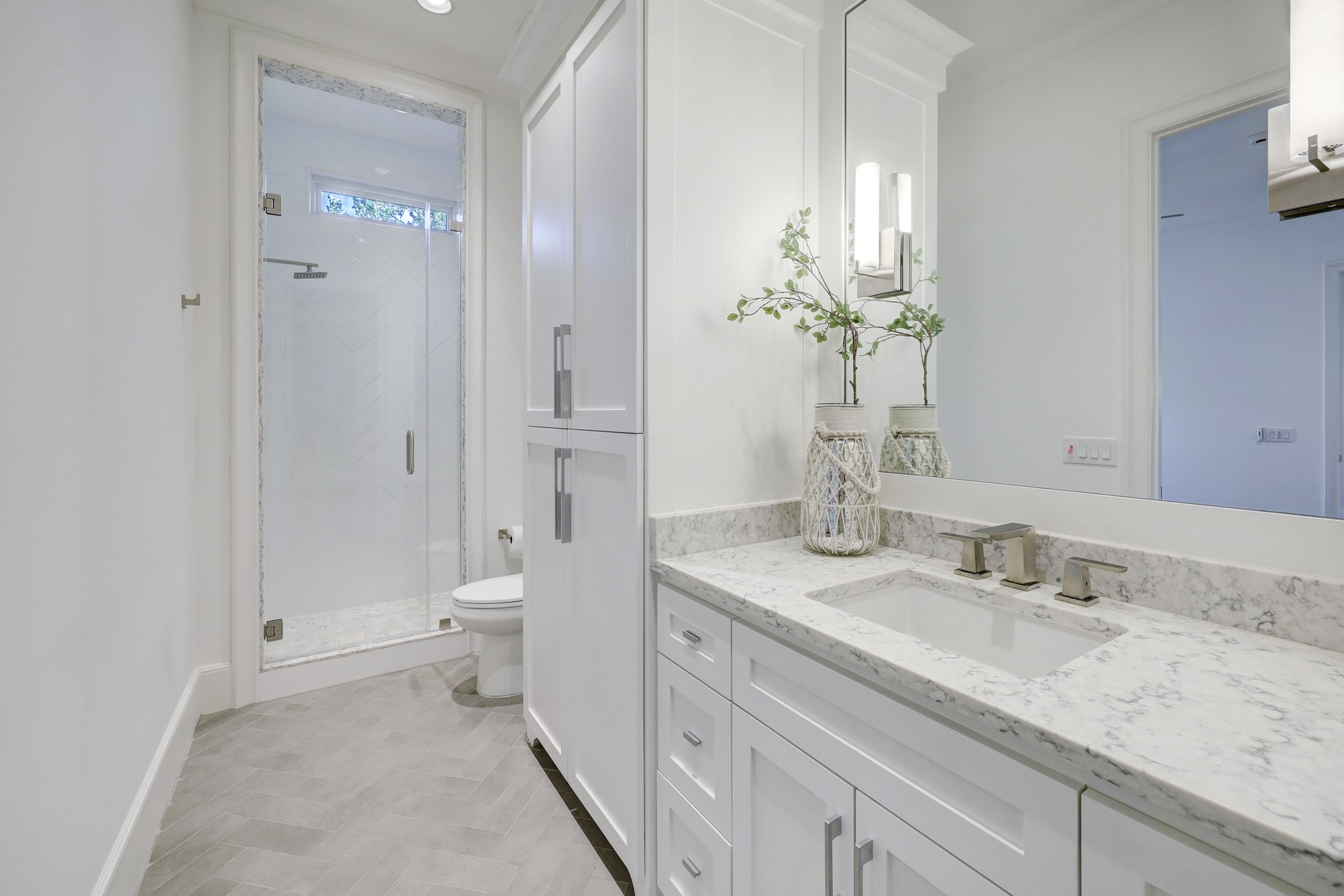 Generously sized guest
bathroom with attractive
herringbone pattern accent tile in shower, transom windows to
allow natural light, and large linen cabinet.