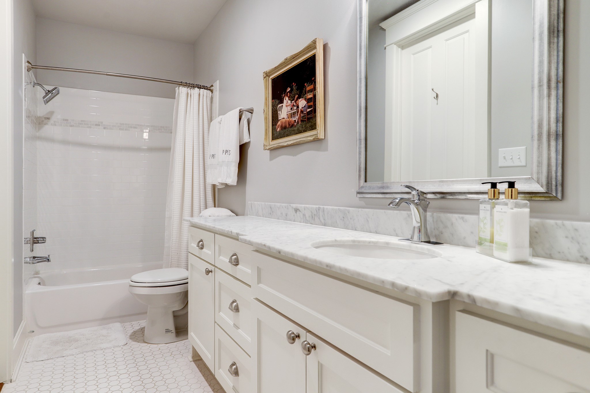 This secondary bathroom features marble counter tops, a shower-bathtub, tile flooring, and hallway access for guests.
