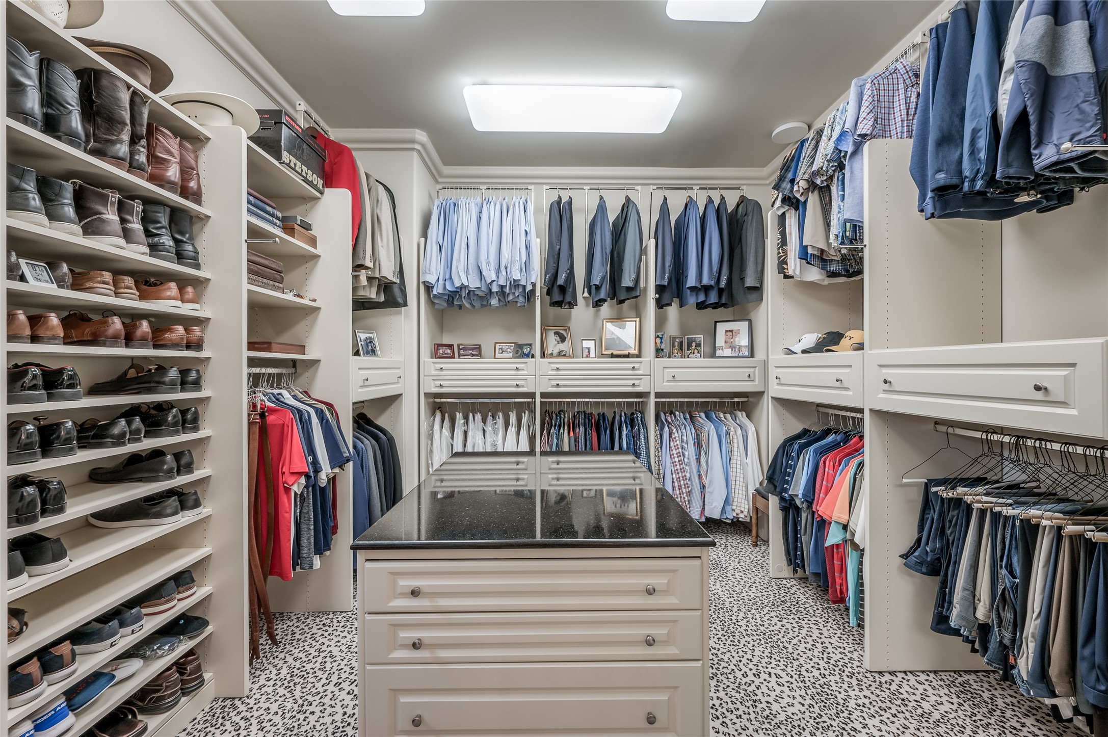 [Primary Closet (1 of 2)
 A pair of bespoke walk-in closets feature packing islands with drawer storage, custom mirrors, and custom-designed storage.