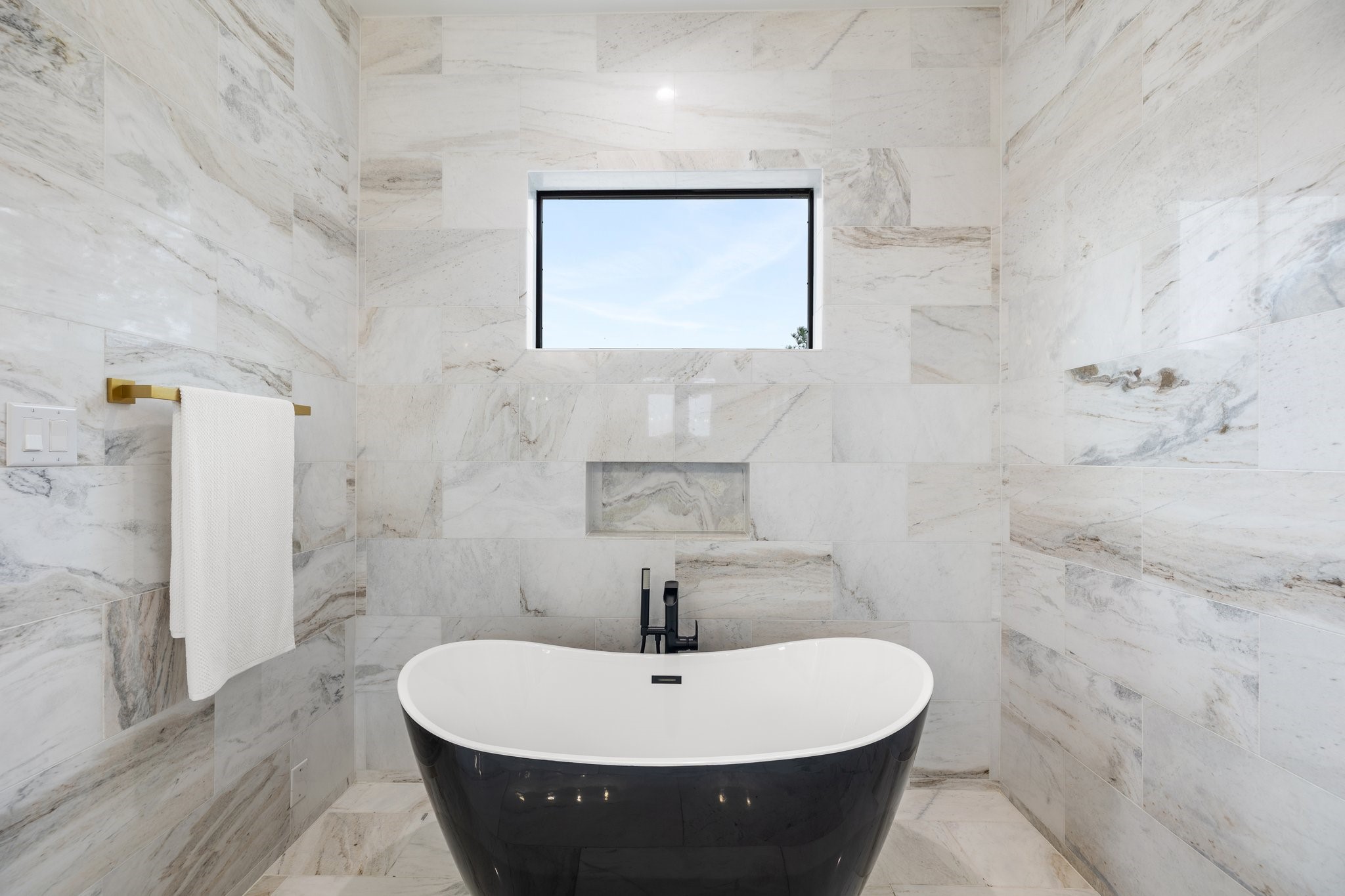 This bold centerpiece takes center stage, inviting you to unwind in luxurious tranquility. Surrounded by floor-to-ceiling tiles and complemented by the sleek design of the space, the black soaking tub stands as an emblem of contemporary refinement.