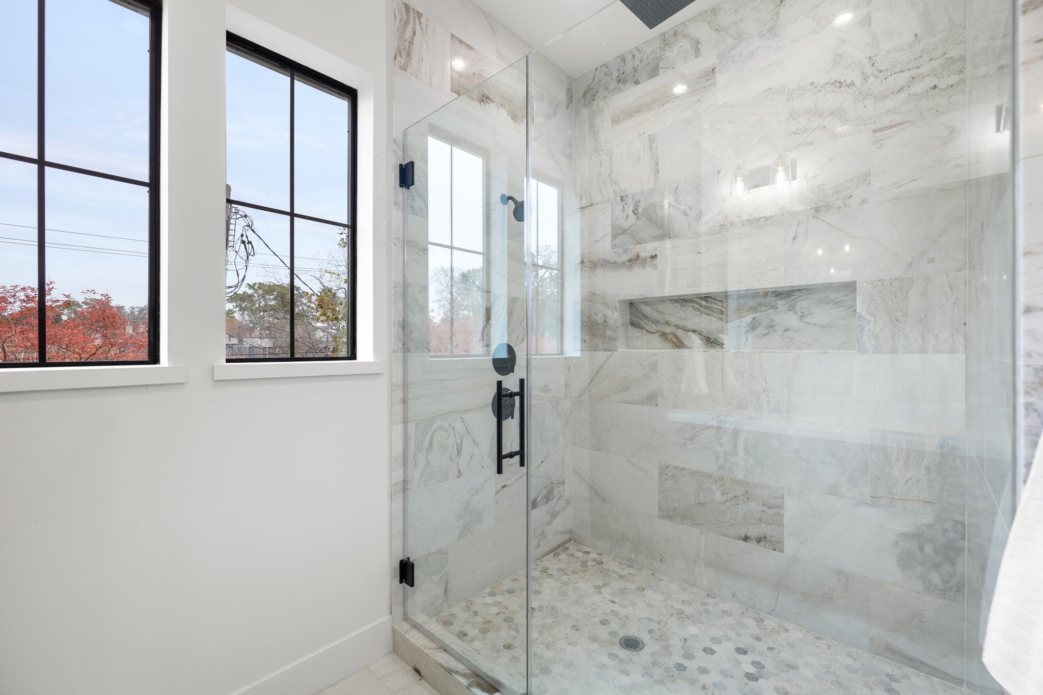 A frameless glass enclosure adorned with sleek black plumbing fixtures. This contemporary touch adds an element of edge and style to your daily routine. An oversized shower niche provides ample space for all your shower essentials.
