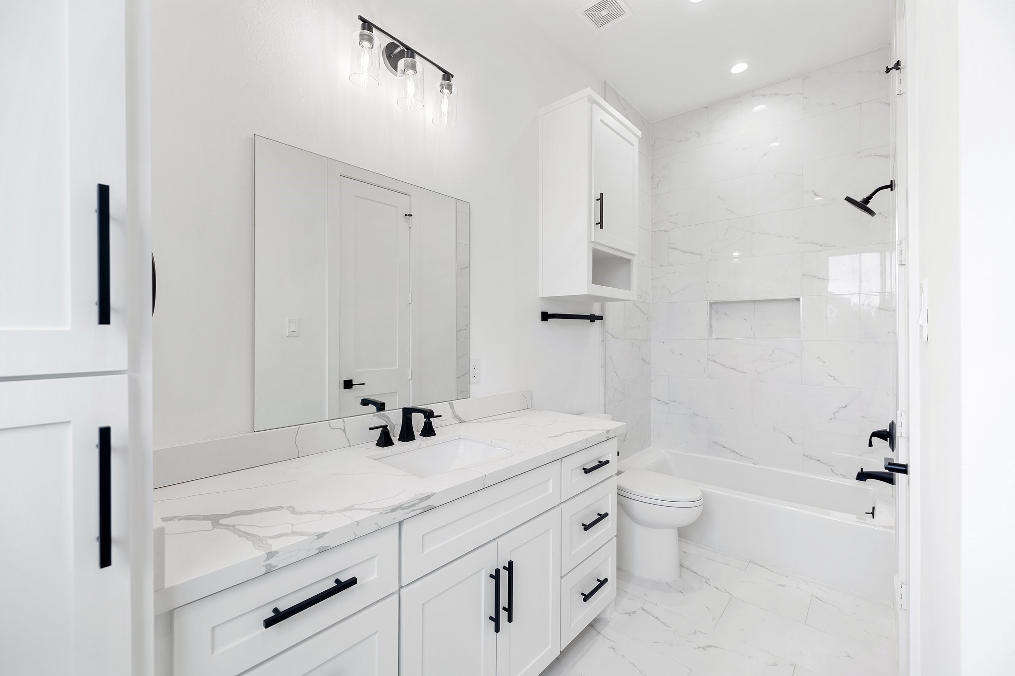 This ensuite bathroom is generously sized with ample cabinet space and an extra countertop for practicality. It features both a shower niche and a tub-shower combo, perfect for the little ones. Beyond, a spacious walk-in closet awaits with additional built-ins, combining functionality and style for your convenience.