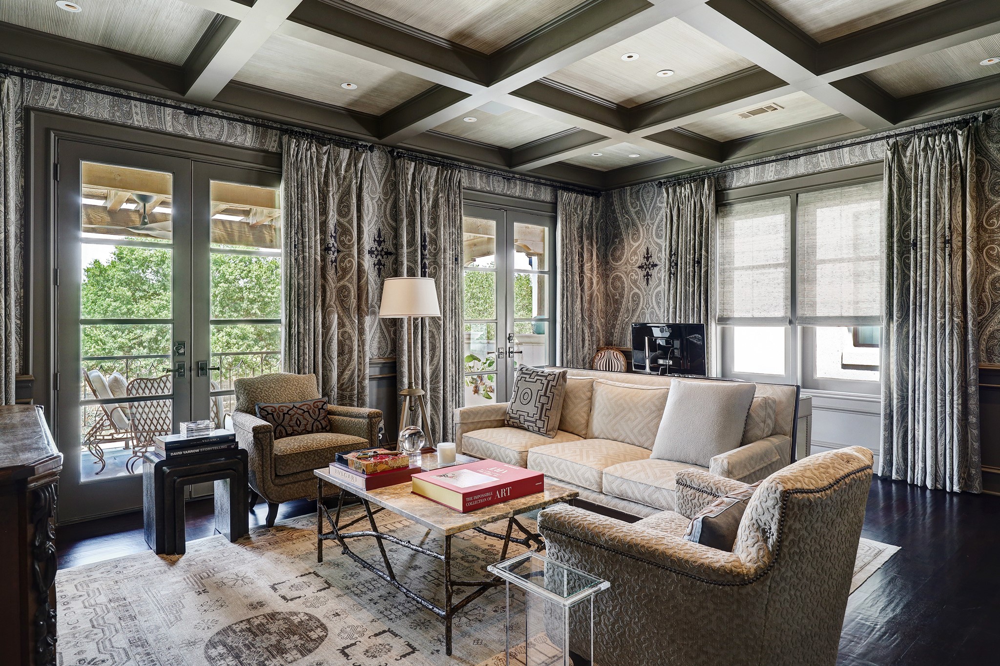 This home office exudes versatility and grandeur yet it retains an allure that hints at potential for relaxation and recreation. Above, the coffered ceilings stand as a testament to architectural brilliance. Elegant fabric-paneled walls encircle the room creating a cocoon of serenity, while the hand-scraped hardwood floors ground the room in authenticity and charm. Two sets of French doors grant access to the upstairs terrace and offer views of the expansive park setting beyond.