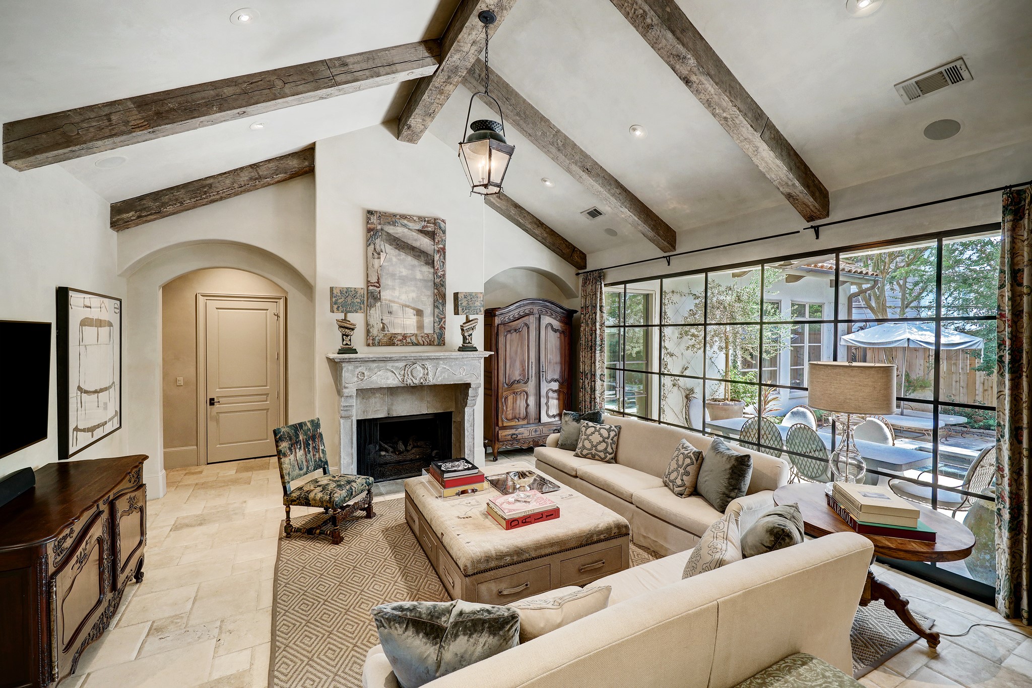 A masterful blend of history and modern luxury, the family room features delicately patinaed 18th-century French stable lanterns and a 16th-century Italian stone fireplace mantle that stands as a testament to Renaissance craftsmanship. Above, reclaimed wooden beams stretch across the ceiling, their rich texture and deep tones adding a touch of rustic charm to the otherwise sophisticated setting.