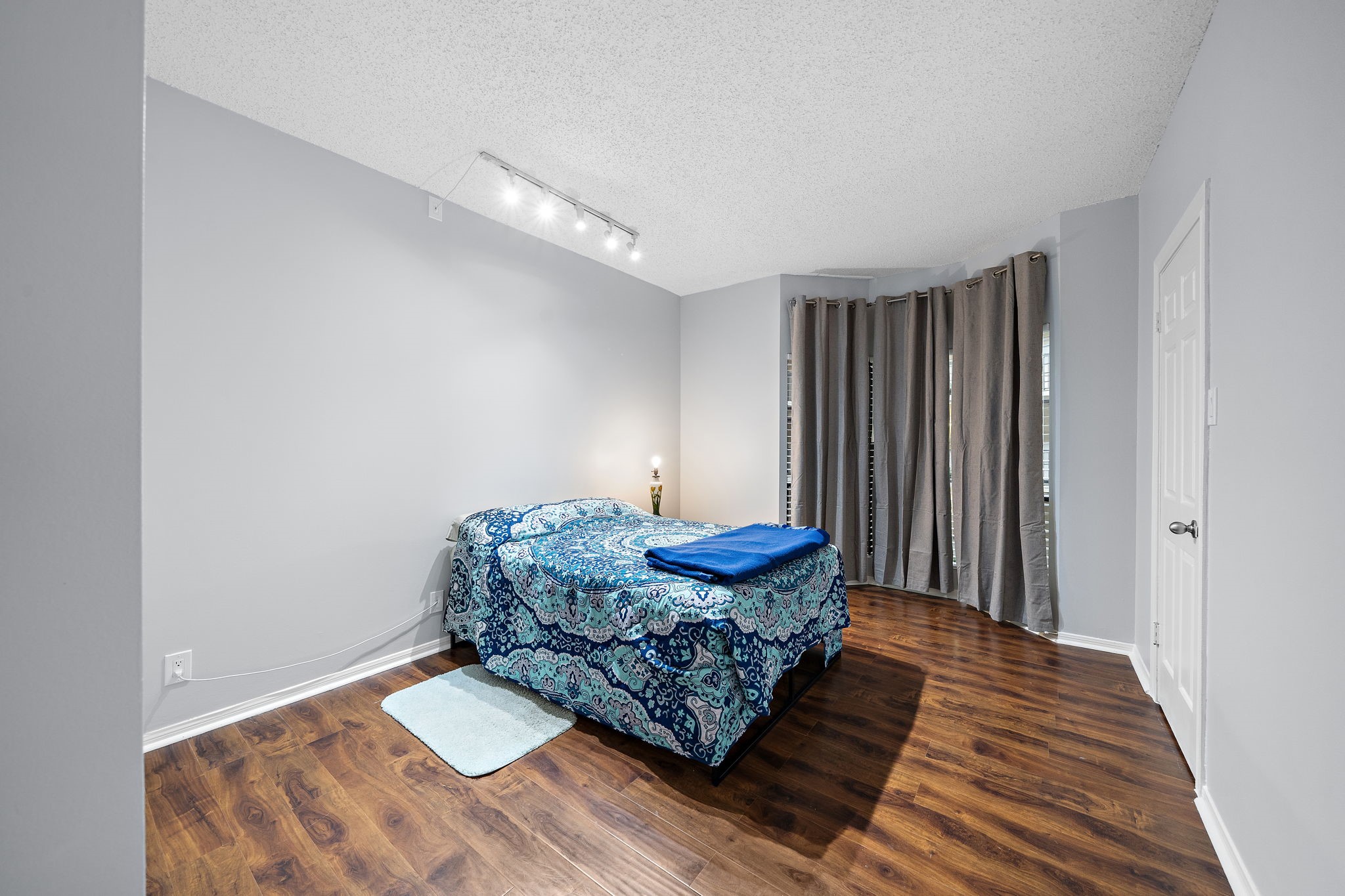Bedroom with hardwood floor, gray walls, spotlighting, draped window, and white door.