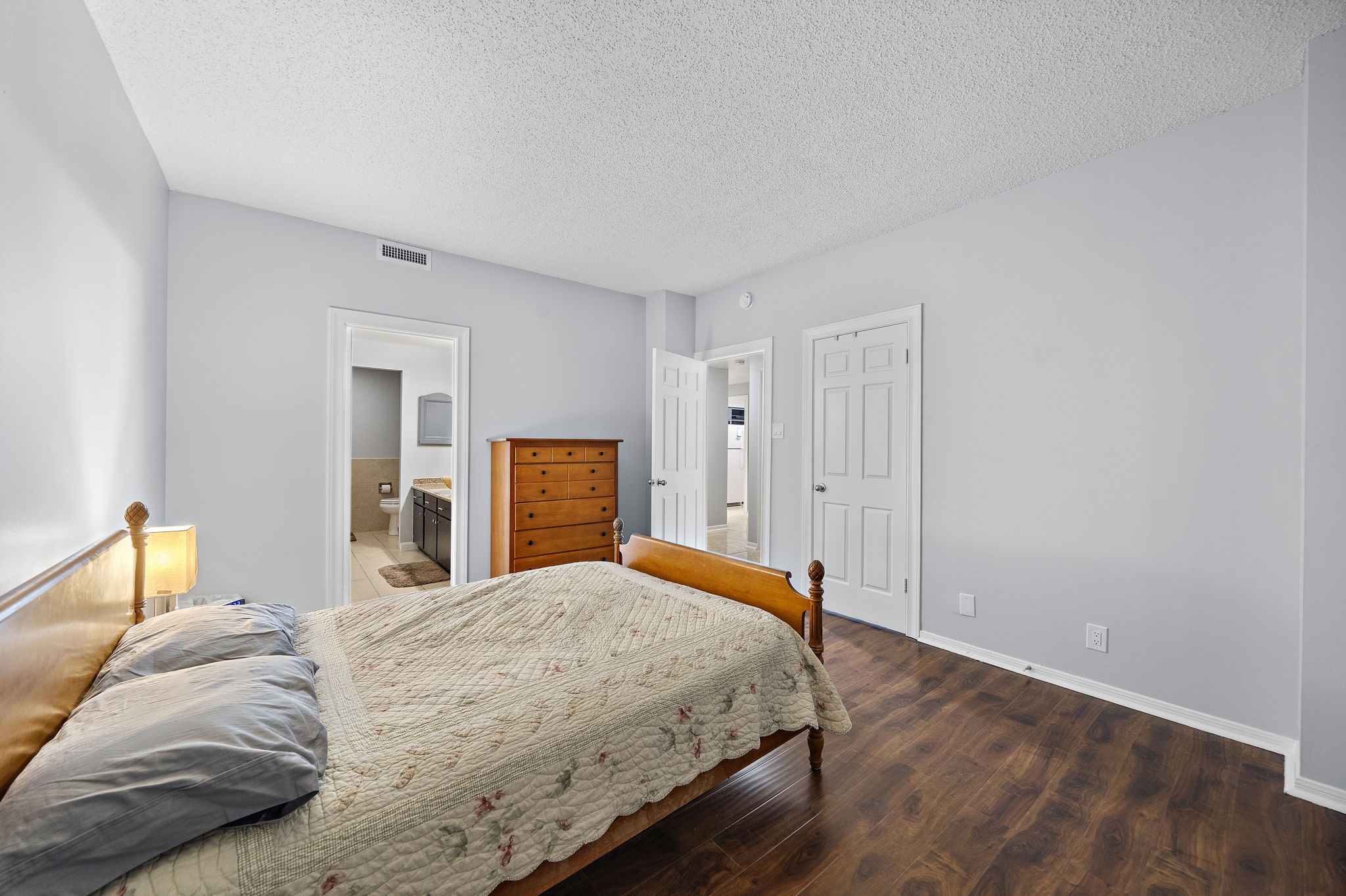 Bedroom with wooden floor, grey walls, two white doors, and a view into another room.
