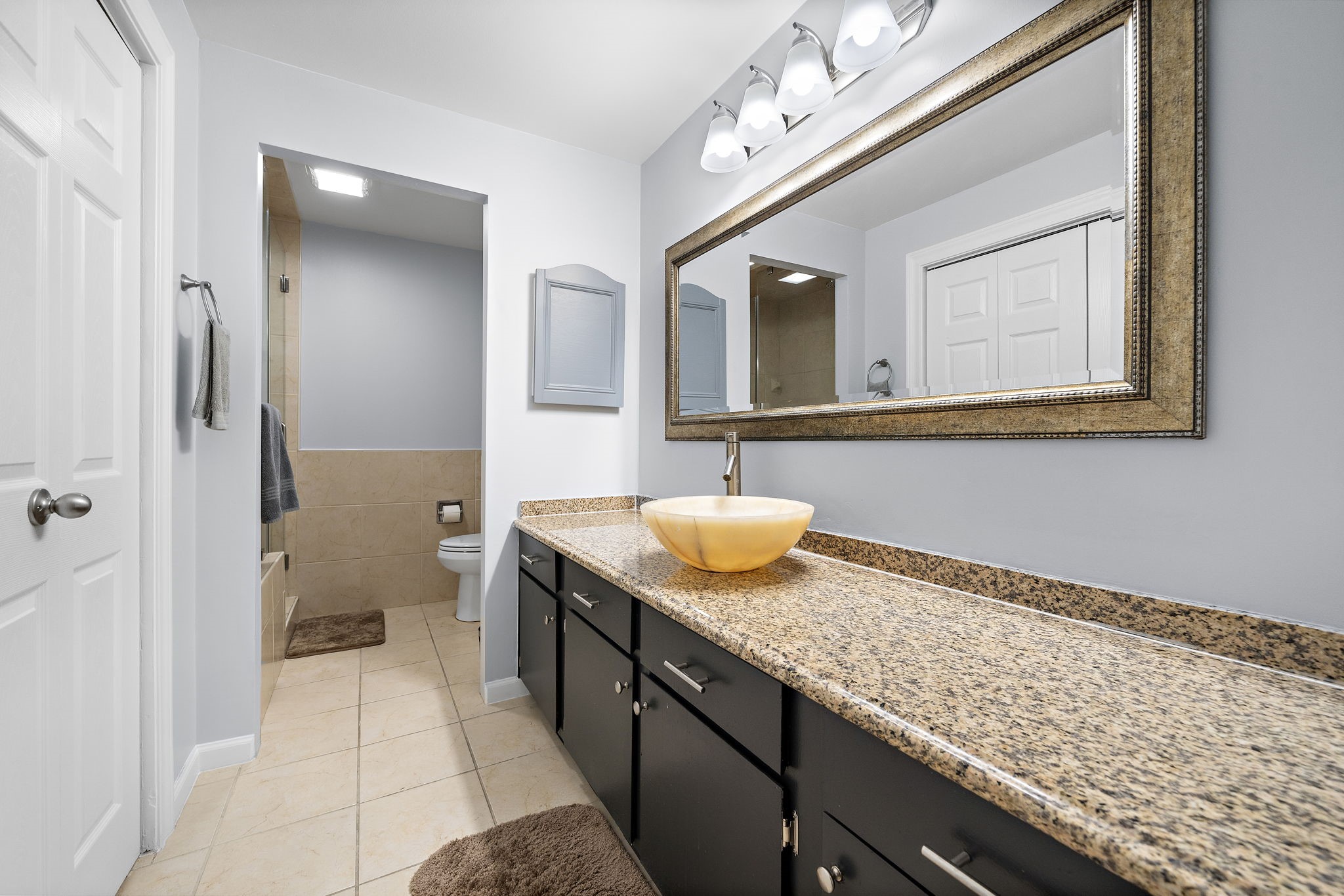 Modern bathroom with dual vanity, granite countertops, large mirror, and a separate toilet area.