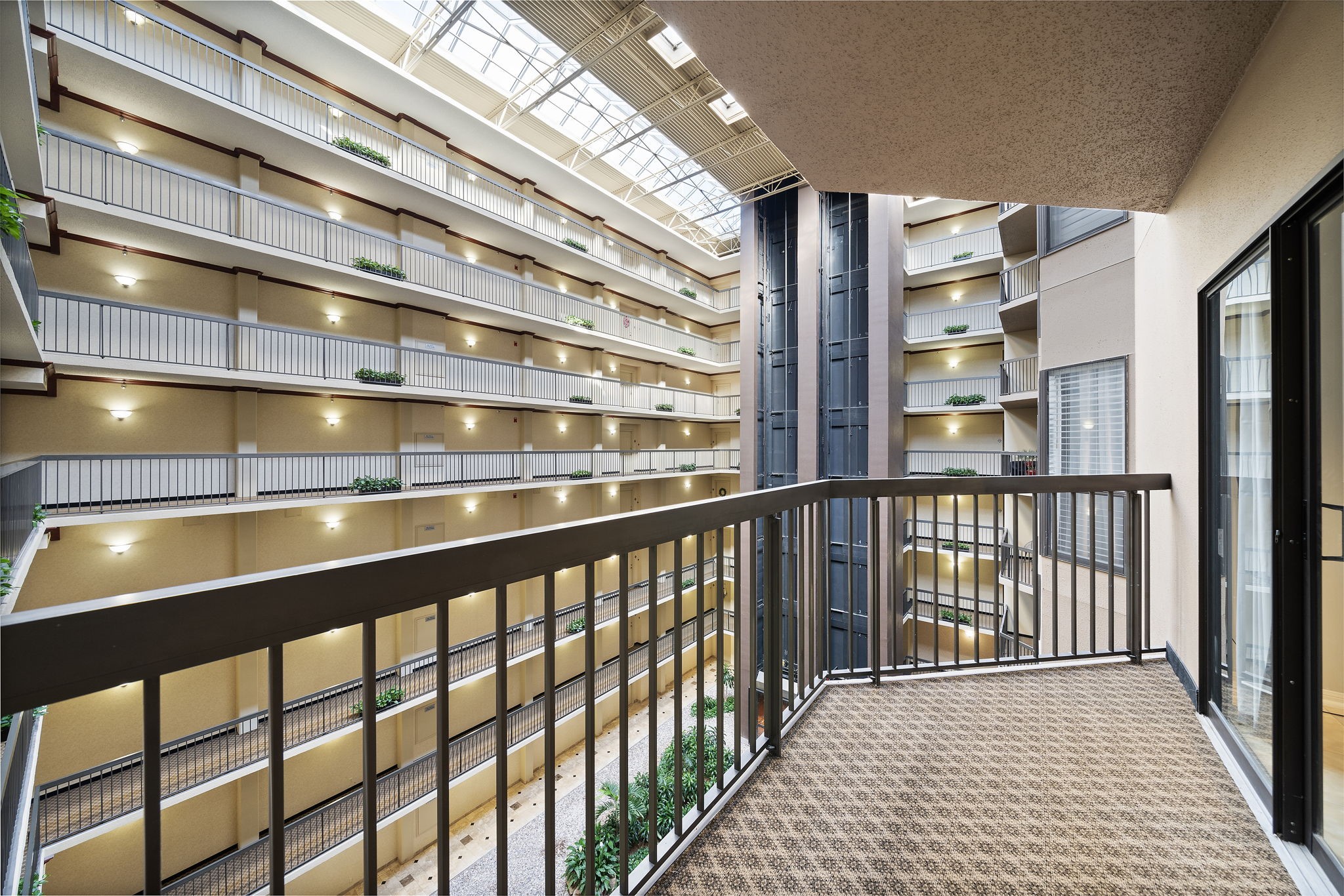 Interior balcony view of a multi-story atrium with natural light and lined with plants.
