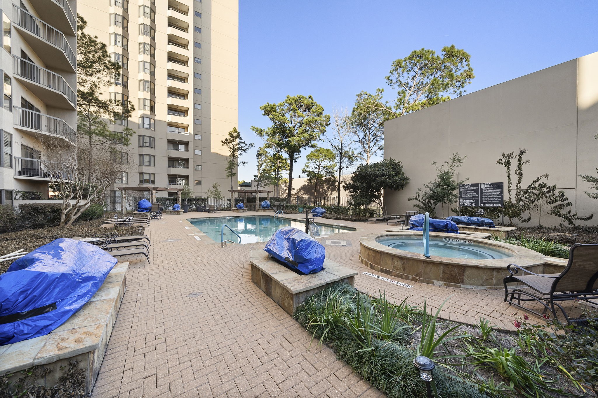 Outdoor pool area with a hot tub, lounge chairs, and a high-rise building in the background.