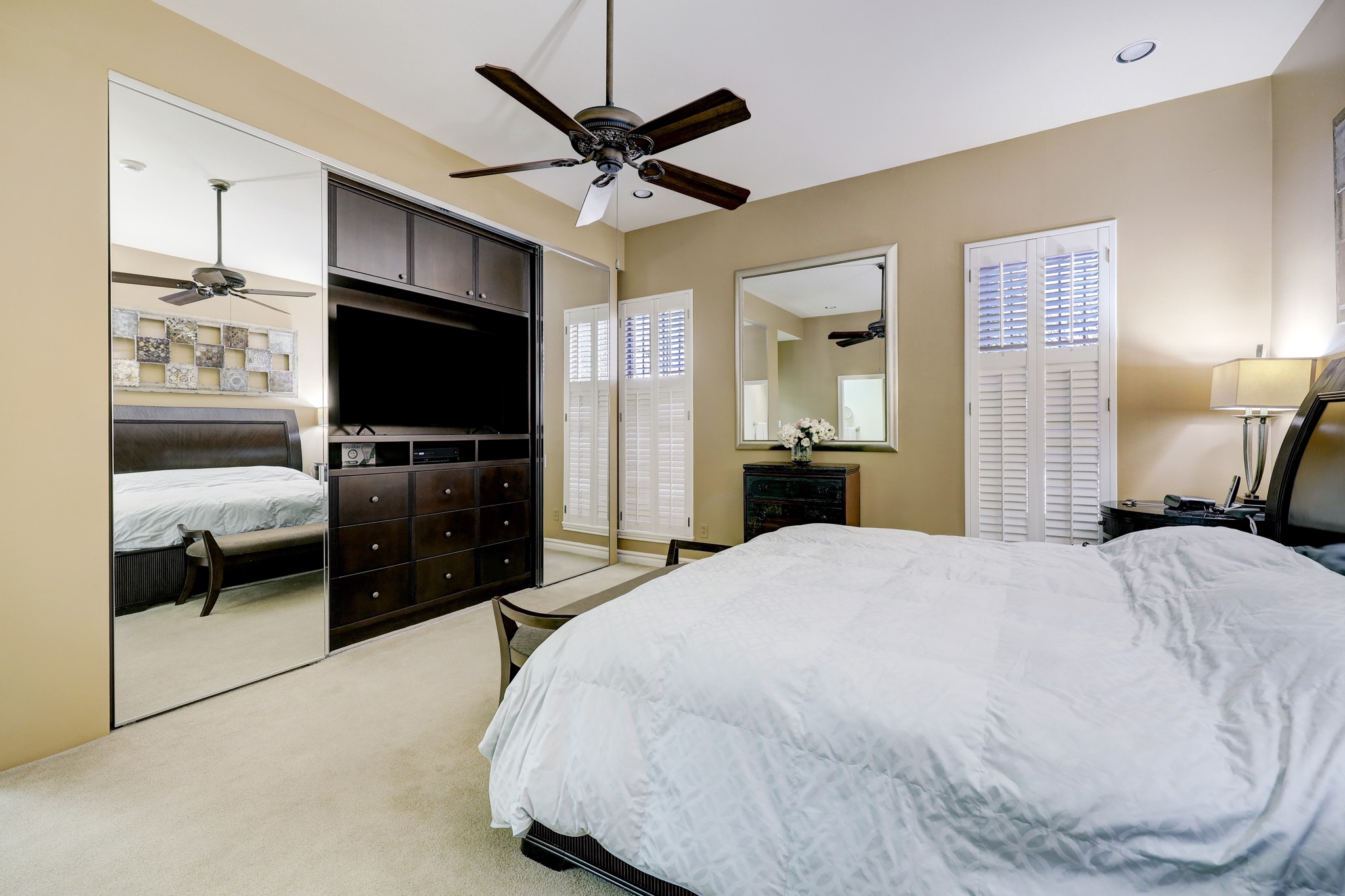 PRIMARY BEDROOM WITH MIRRORED SLIDING DOORS CONCEALING BUILT IN STORAGE AND ENTERTAINMENT CENTER