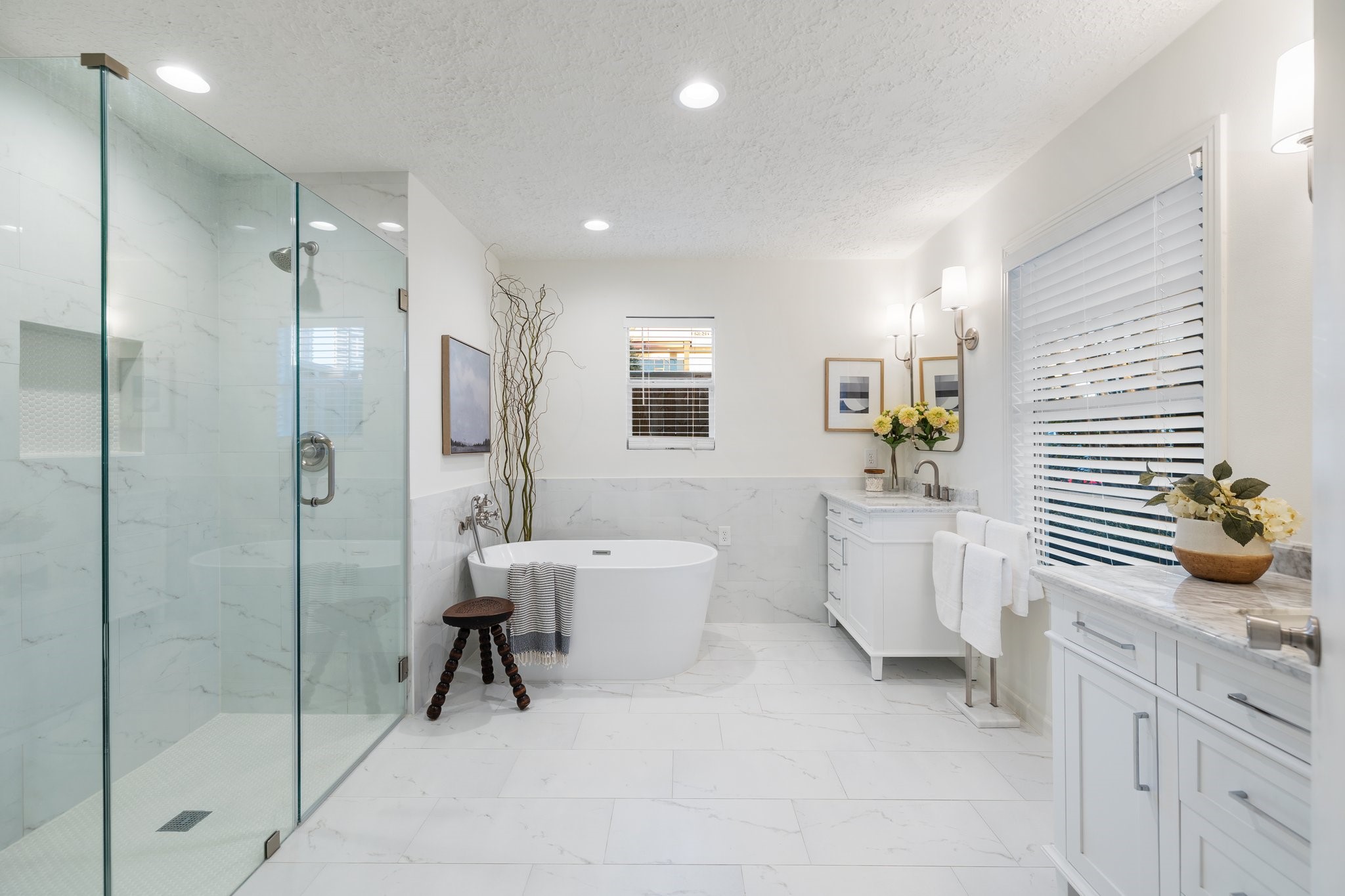 The master bath has undergone a substantial transformation, featuring a soaking tub, a glass-framed shower with a custom niche, dual marble vanities, custom sconces, mirrors, brushed nickel faucets, and exquisite tile flooring.