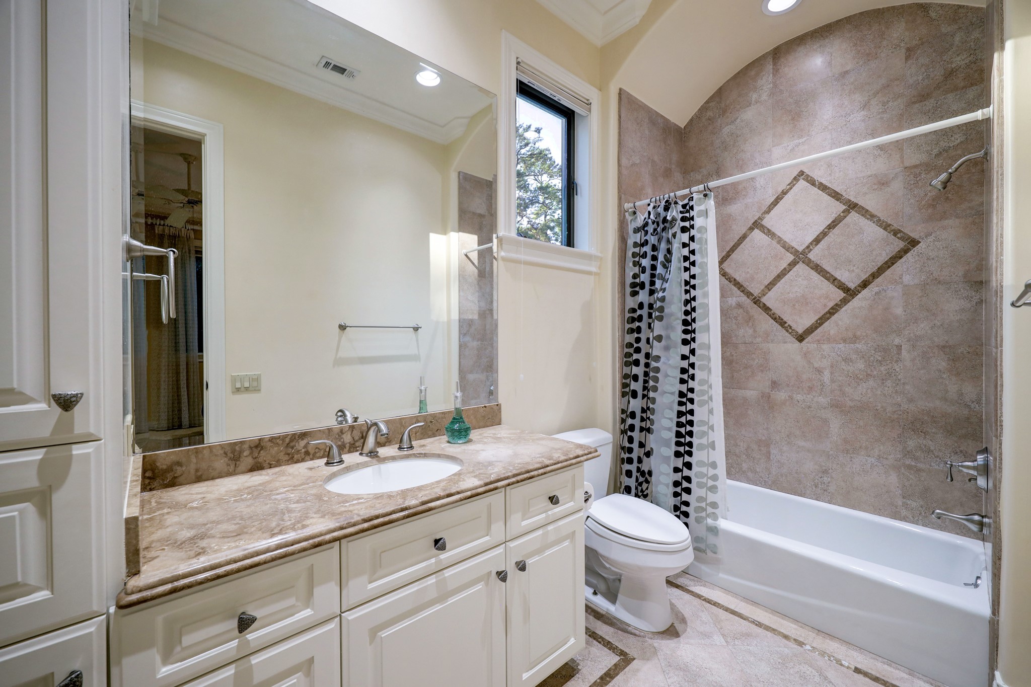 This Secondary Bathroom [11 x 5] features tile floors, marble countertop and backsplash, built-in linen storage and laundry hamper, and tub/shower combo with tile surround.