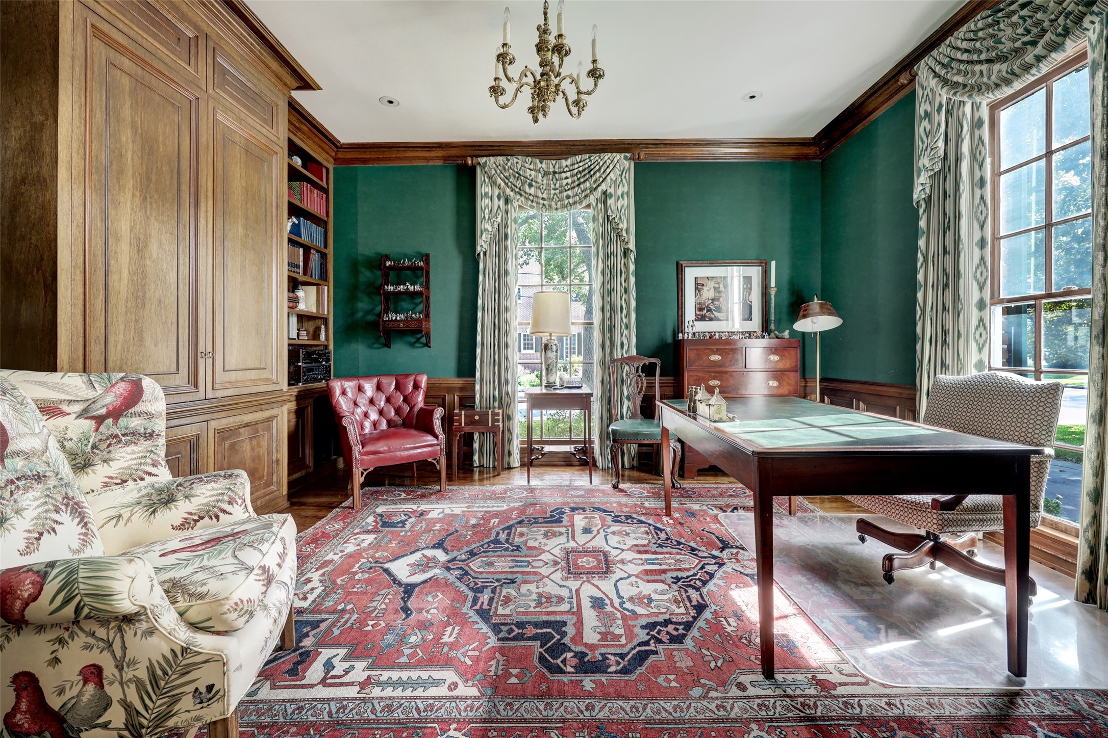 The stately library/home office boasts built-in shelves and drawers as well as large windows that frame views of the front gardens and infuse the room with natural light and a serene atmosphere.