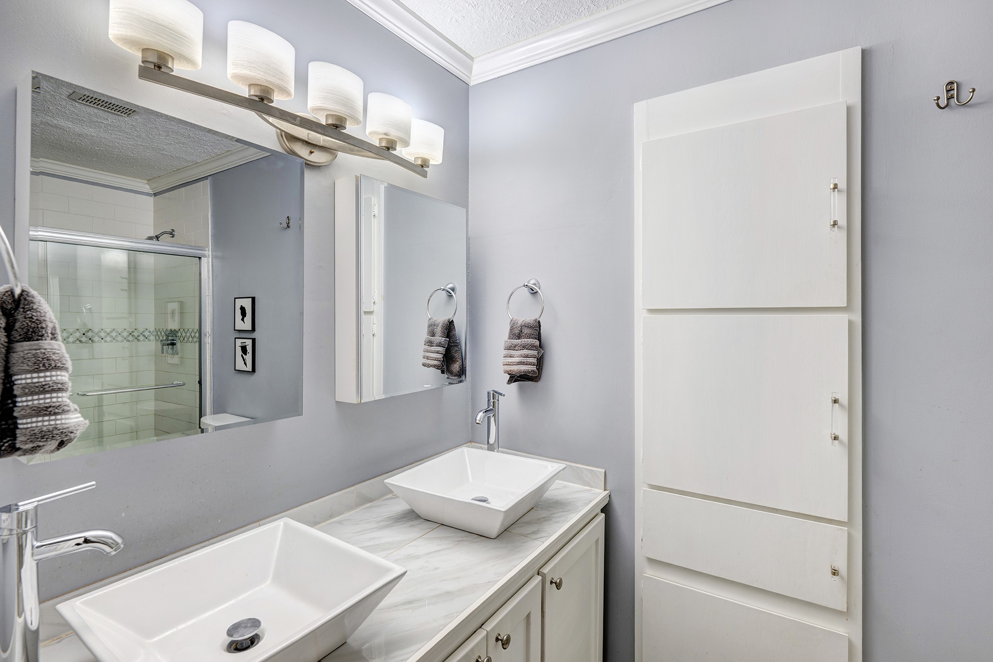 The remodeled primary bathroom showcases a sophisticated dual vanity equipped with exquisite lighting and a spacious walk-in shower enclosed by a sleek sliding glass door.