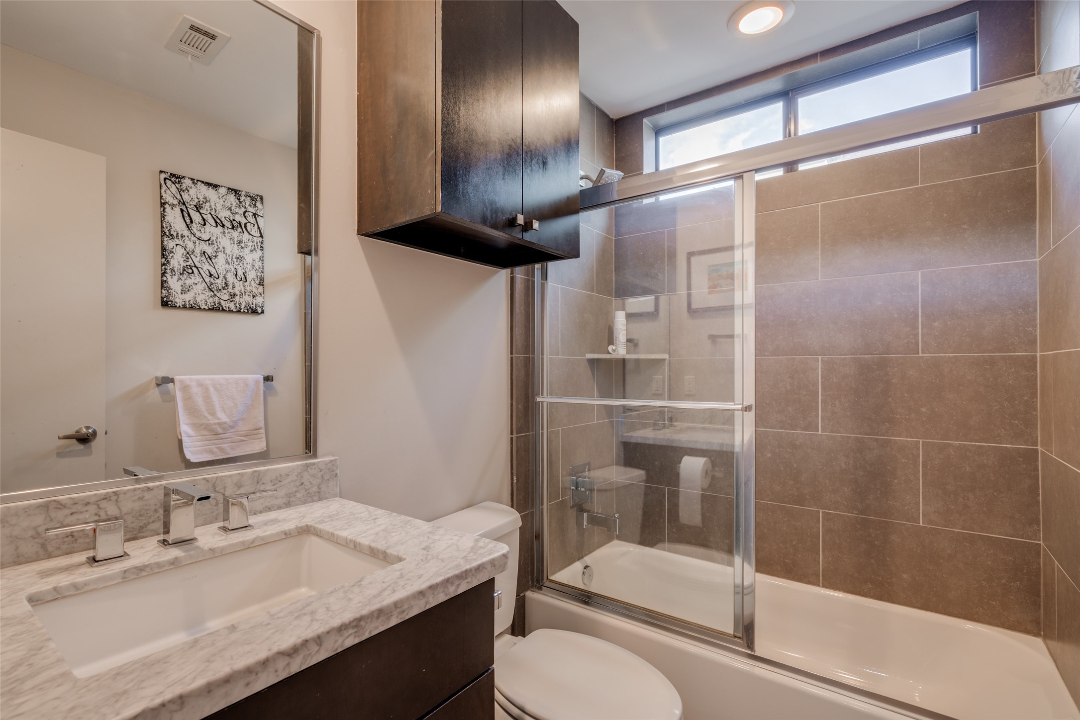 Bathroom 3 with gray floor & tub tile with shower surround, beautiful Carrera marble counter with under mounted sink, frameless mirror, dark expresso cabinet