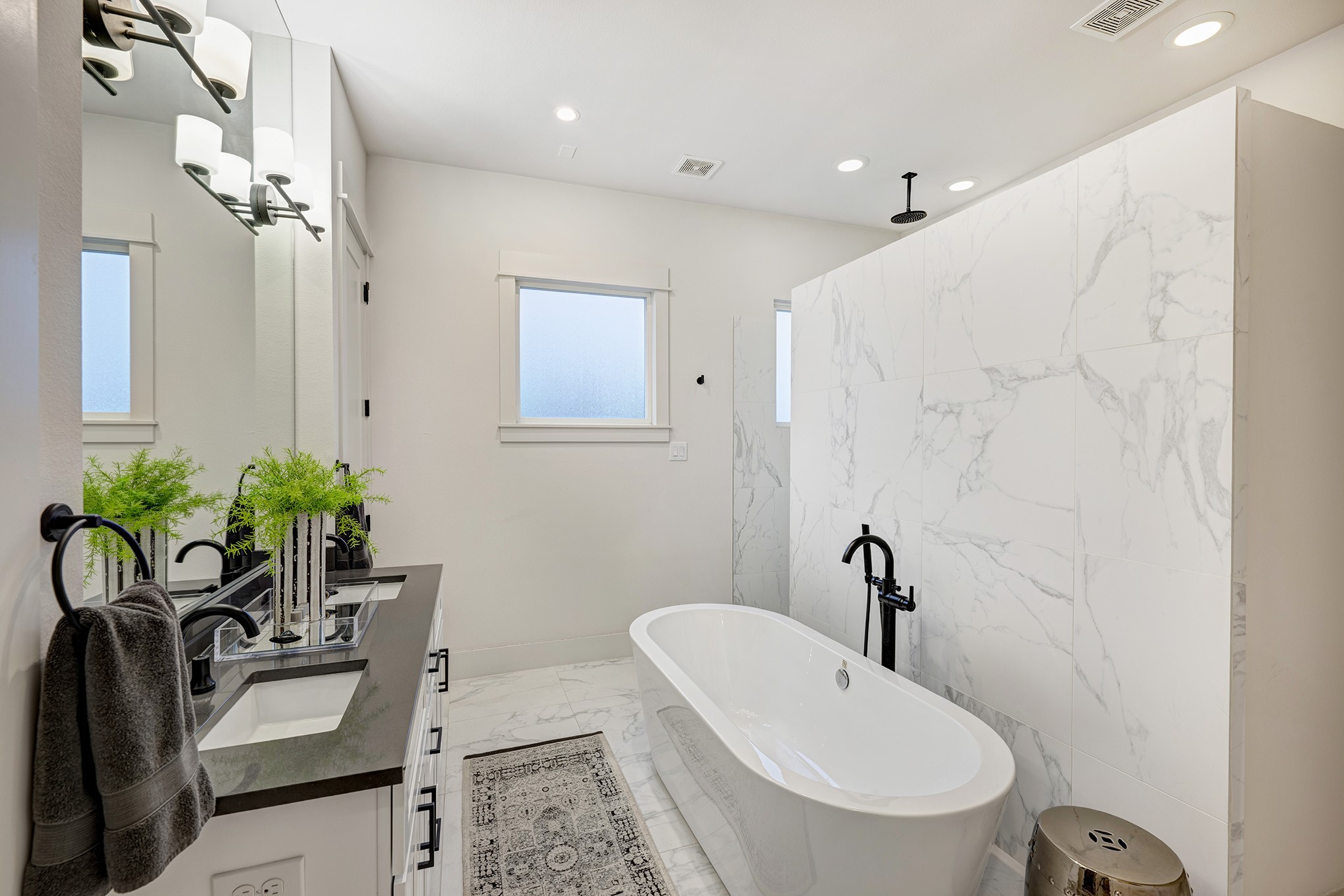 Luxurious primary bathroom has a spa-like feel with quartz counter, double sinks, freestanding soaking tub and linen closet.