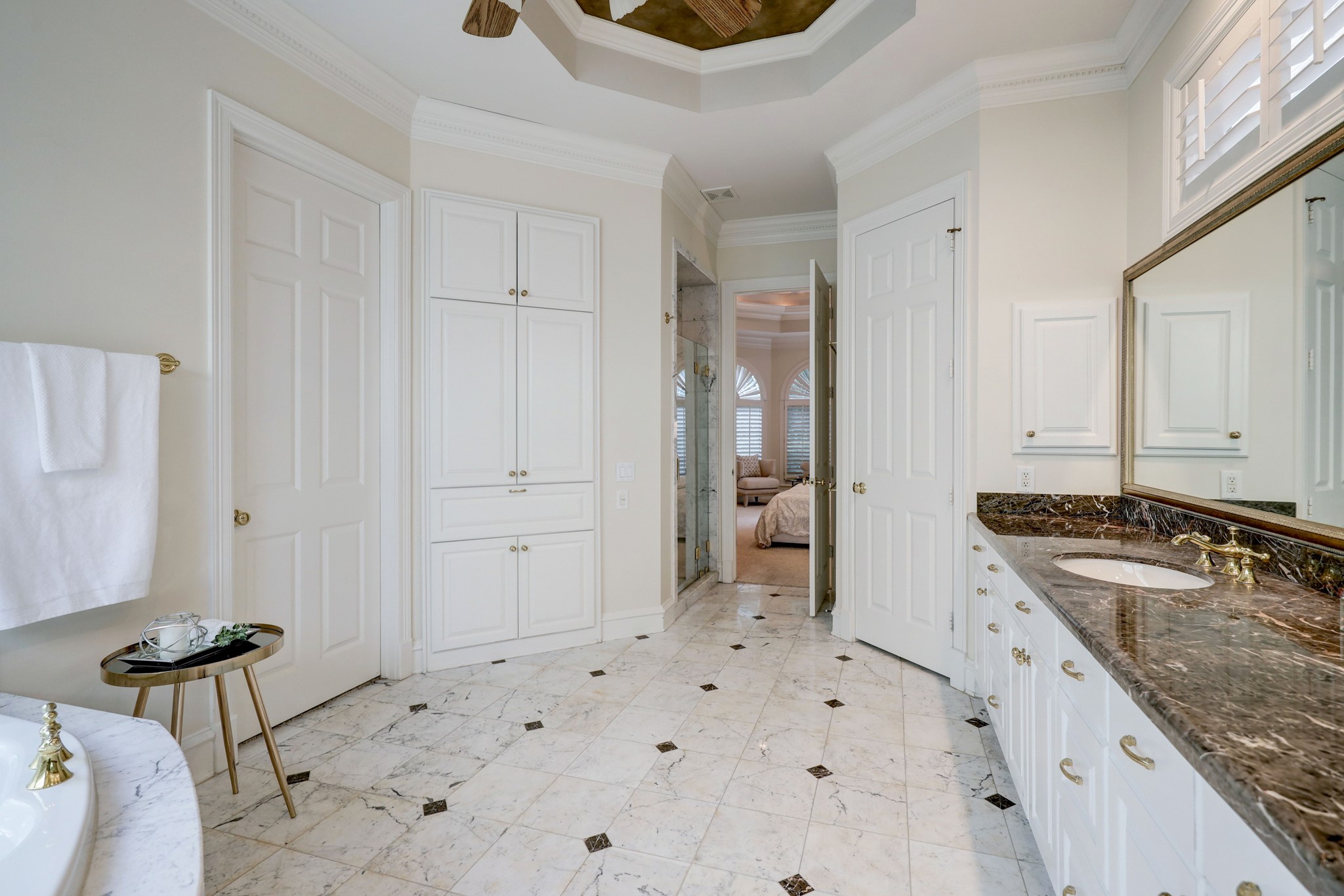 This view shows the Primary Bath looking back into the Primary Suite.  On the right side beyond the vanity area is the enclosed water closet. On the left is the door to the very large walk-in closet and then generous built-ins for towels, sundries, and a hamper.  Behind the built-ins is the separate marble shower.