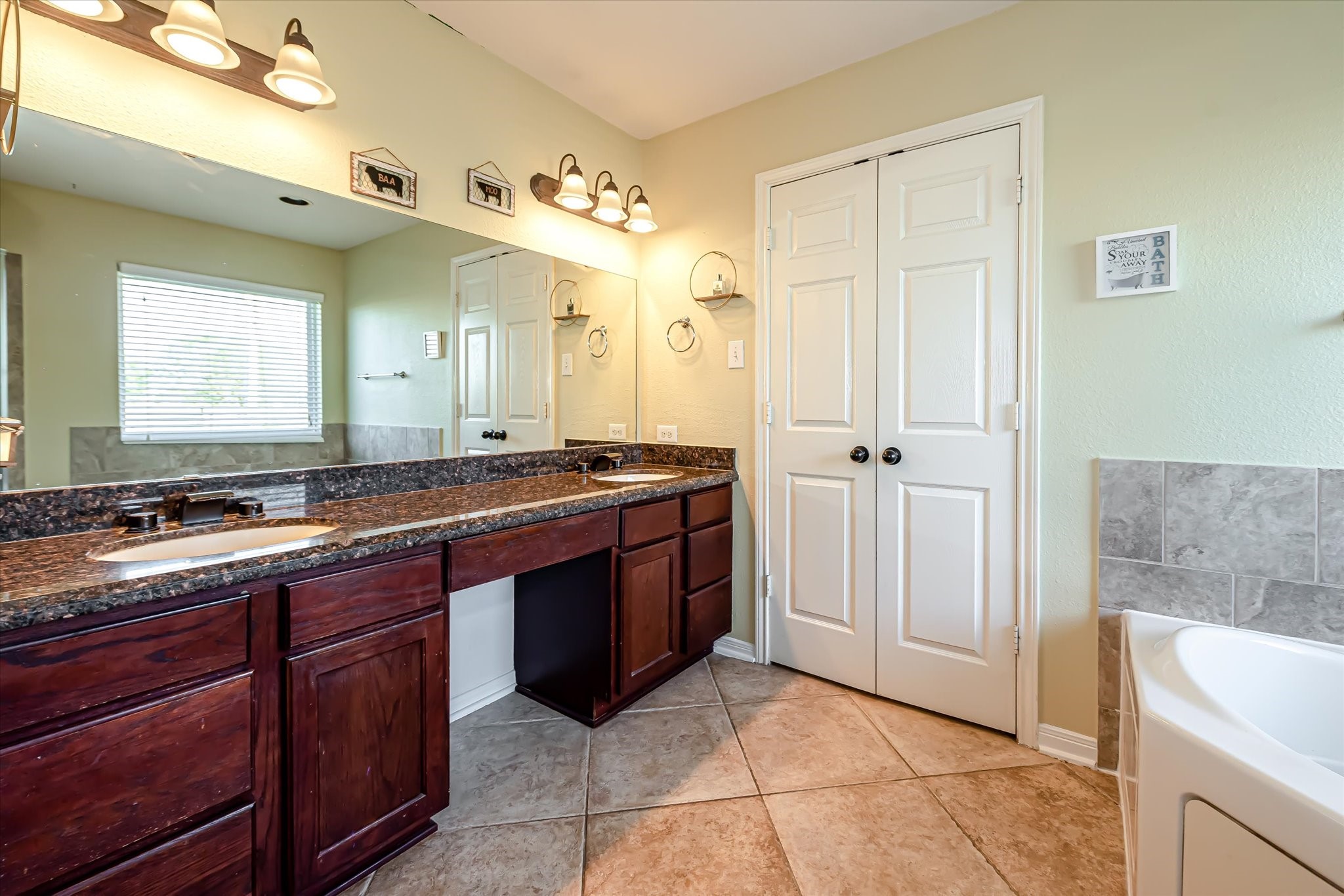 Primary bath has tile floor, granite counter, two sinks and seated vanity.