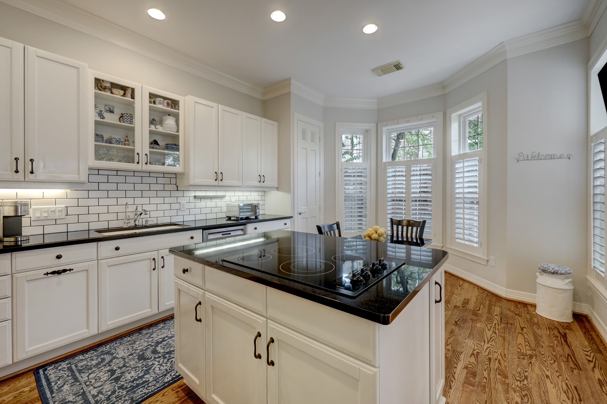 The updated kitchen features black granite countertops, white cabinetry, and striking white subway tile with black grout.  The door in the rear of the photo opens to the pantry.