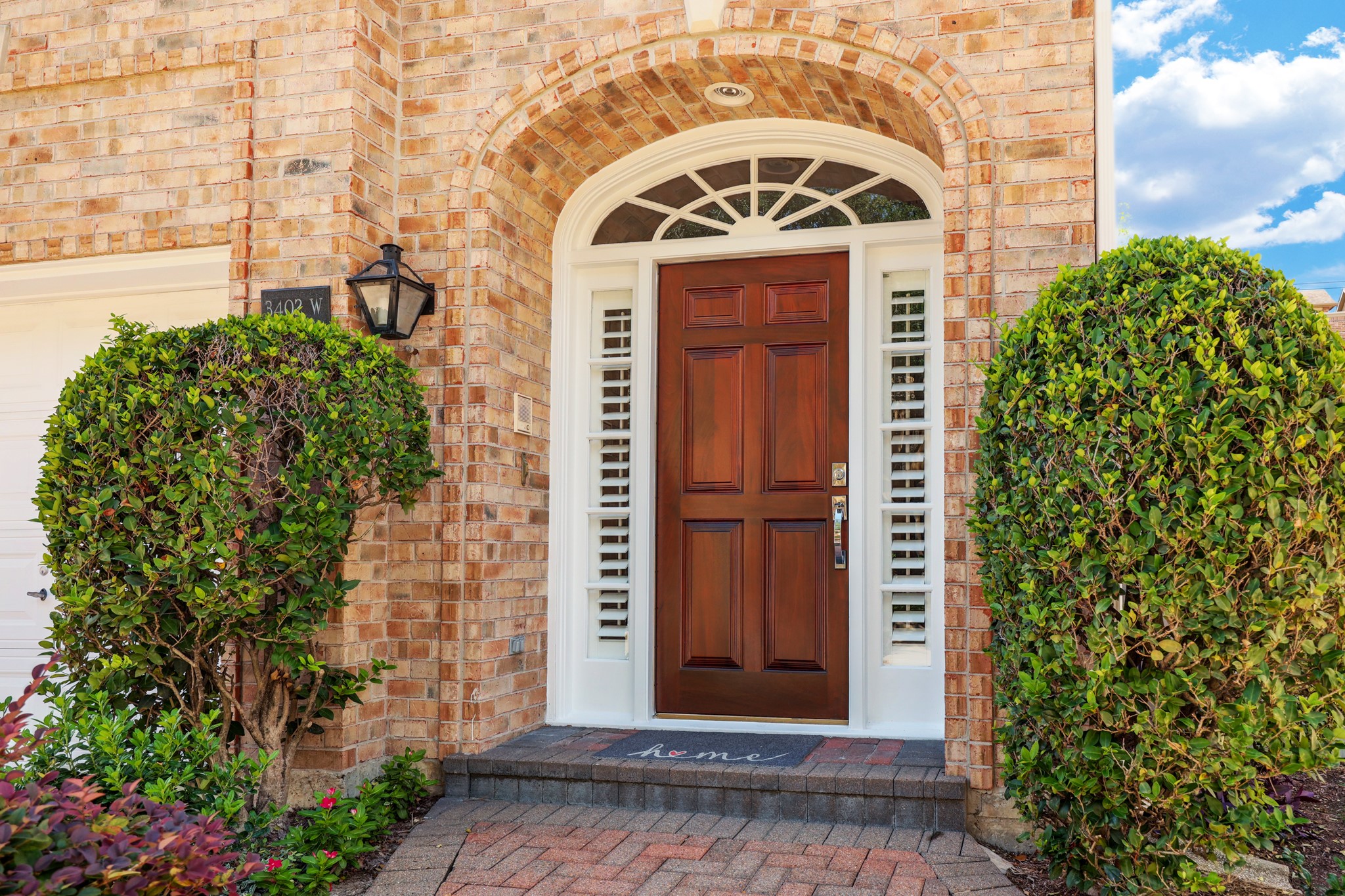 The freshly painted and attractive front door and surround are flanked by beds with shrubs and flowers.